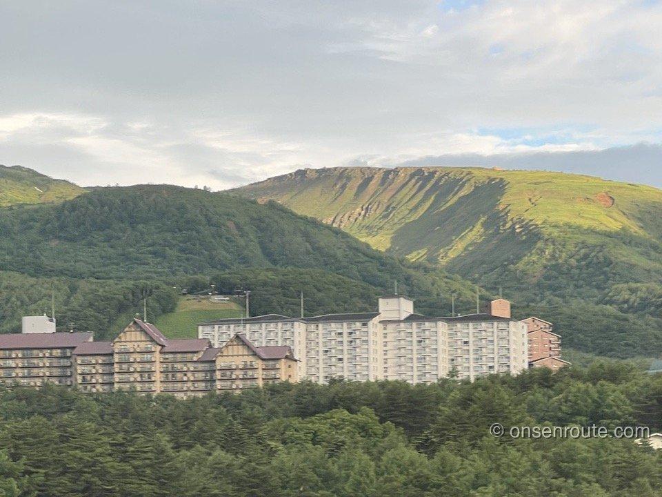 部屋の窓から見た草津の山並み。緑の森の向こうに山肌とリゾートマンション群が見える