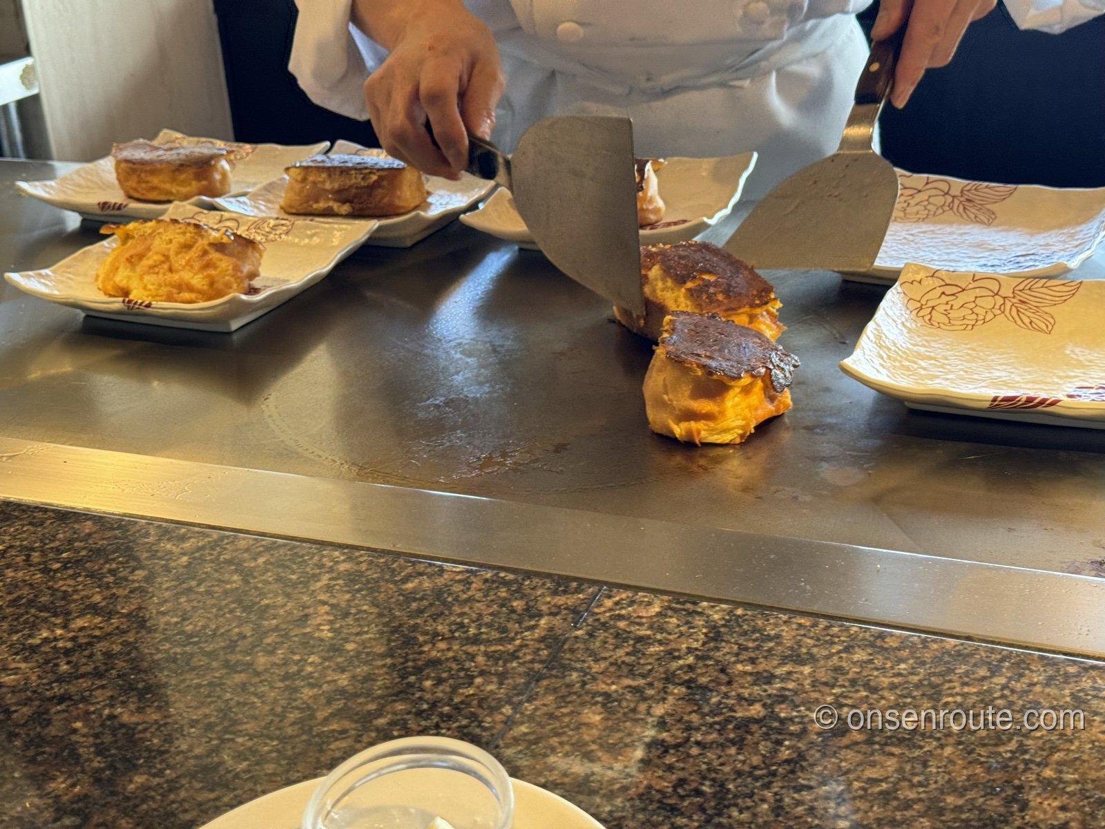 鉄板ブレークファースト。料理人が鉄板の上で焼き上げた一品を切り分けている