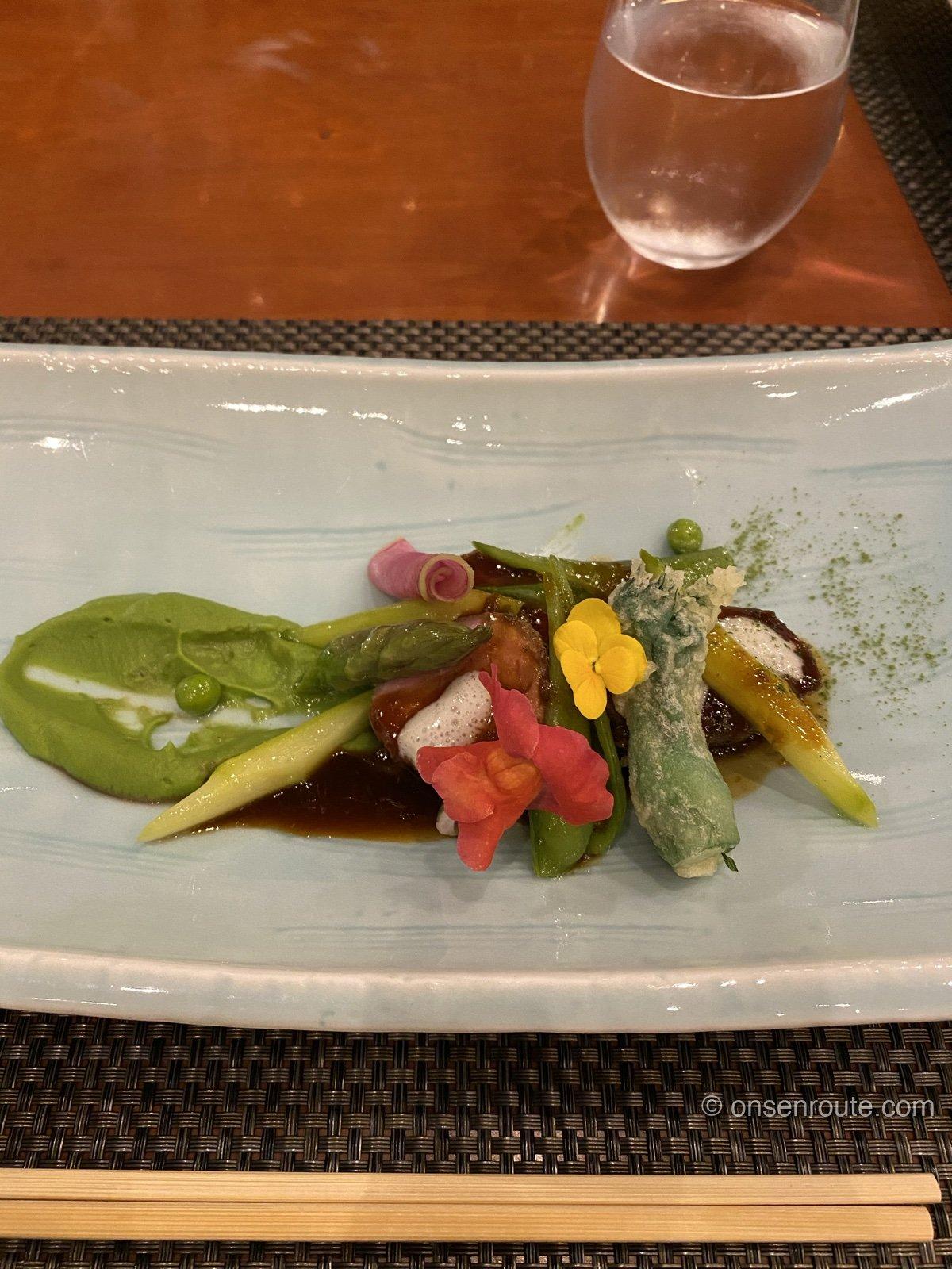 夕食のメイン料理。青い長皿にアスパラガスやエディブルフラワーが彩りよく盛り付けられている