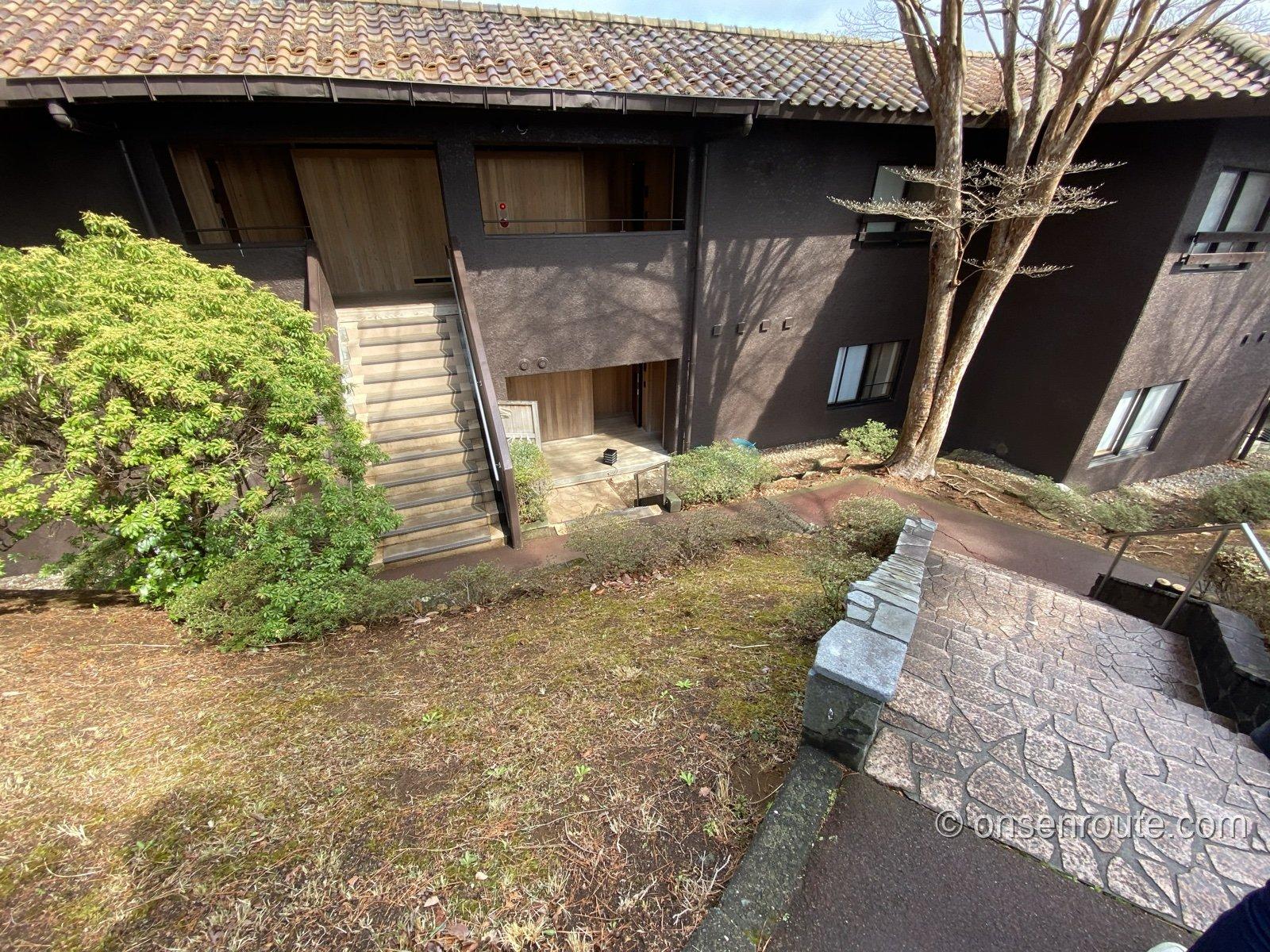 山紫水明の建物の外観。木々に囲まれた焦げ茶色の低層の建物に石畳の小道が続く