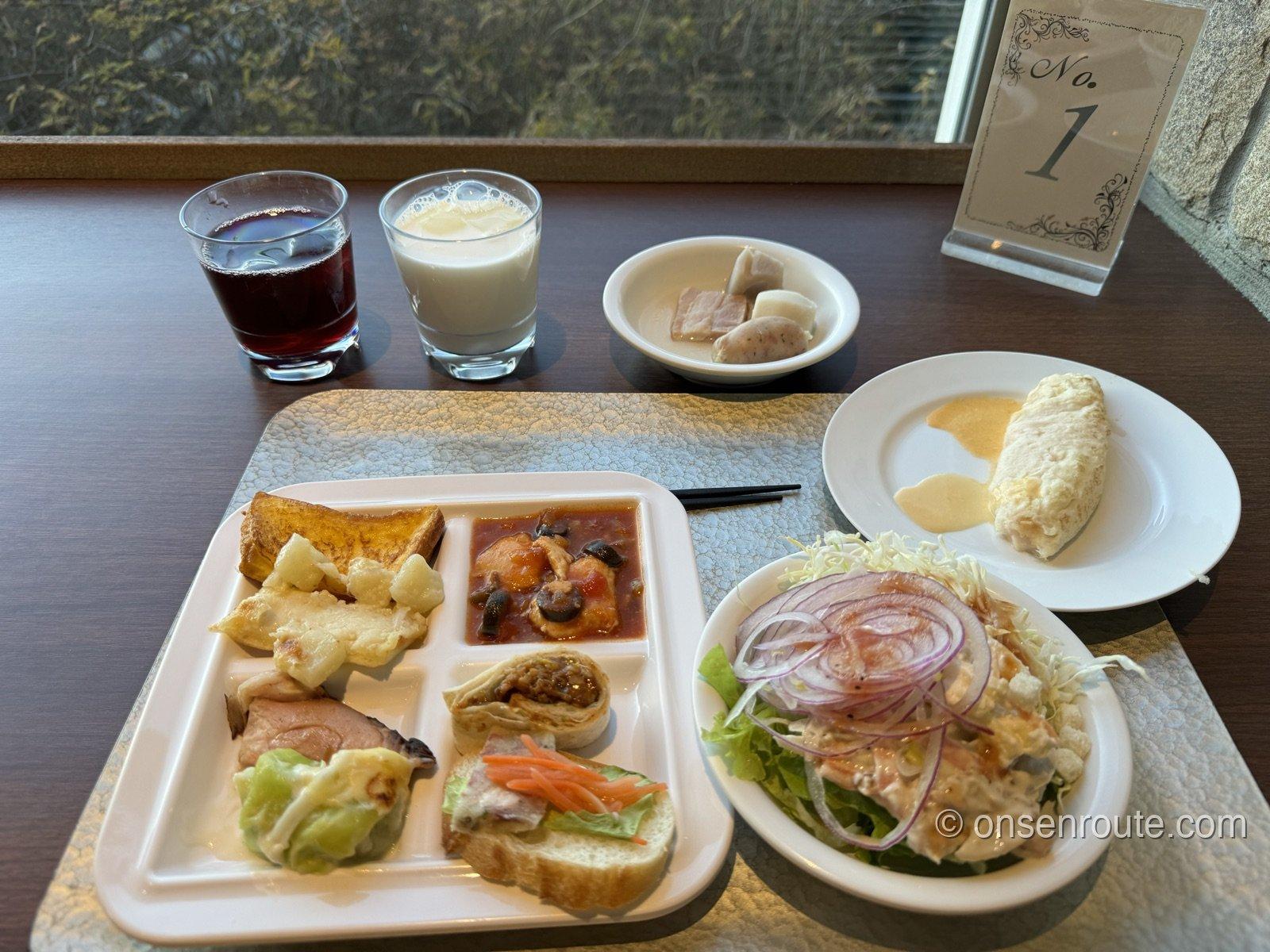 朝食ビュッフェのトレー。フレンチトースト、サラダ、オムレツ、葡萄ジュースと牛乳が並ぶ