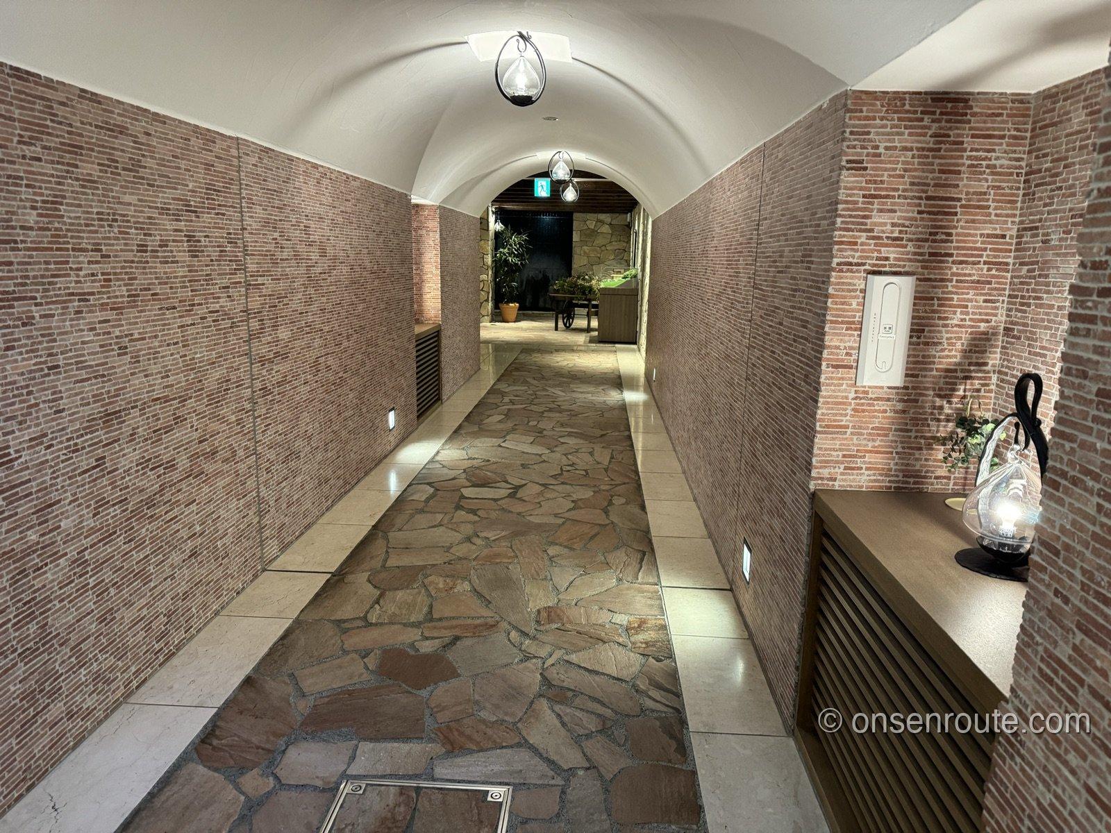 レンガ張りの壁とアーチ天井が続く館内廊下。石畳風の床にランタン風の照明が灯る