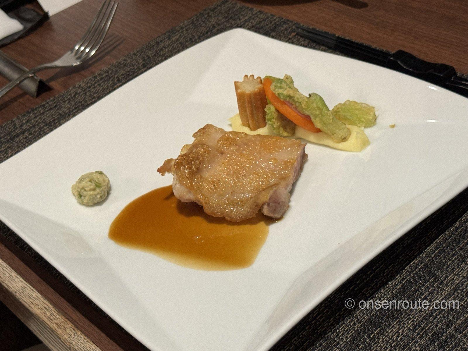 白い角皿に盛られた鶏肉のロースト。ソースと彩り野菜の天ぷらが添えられている