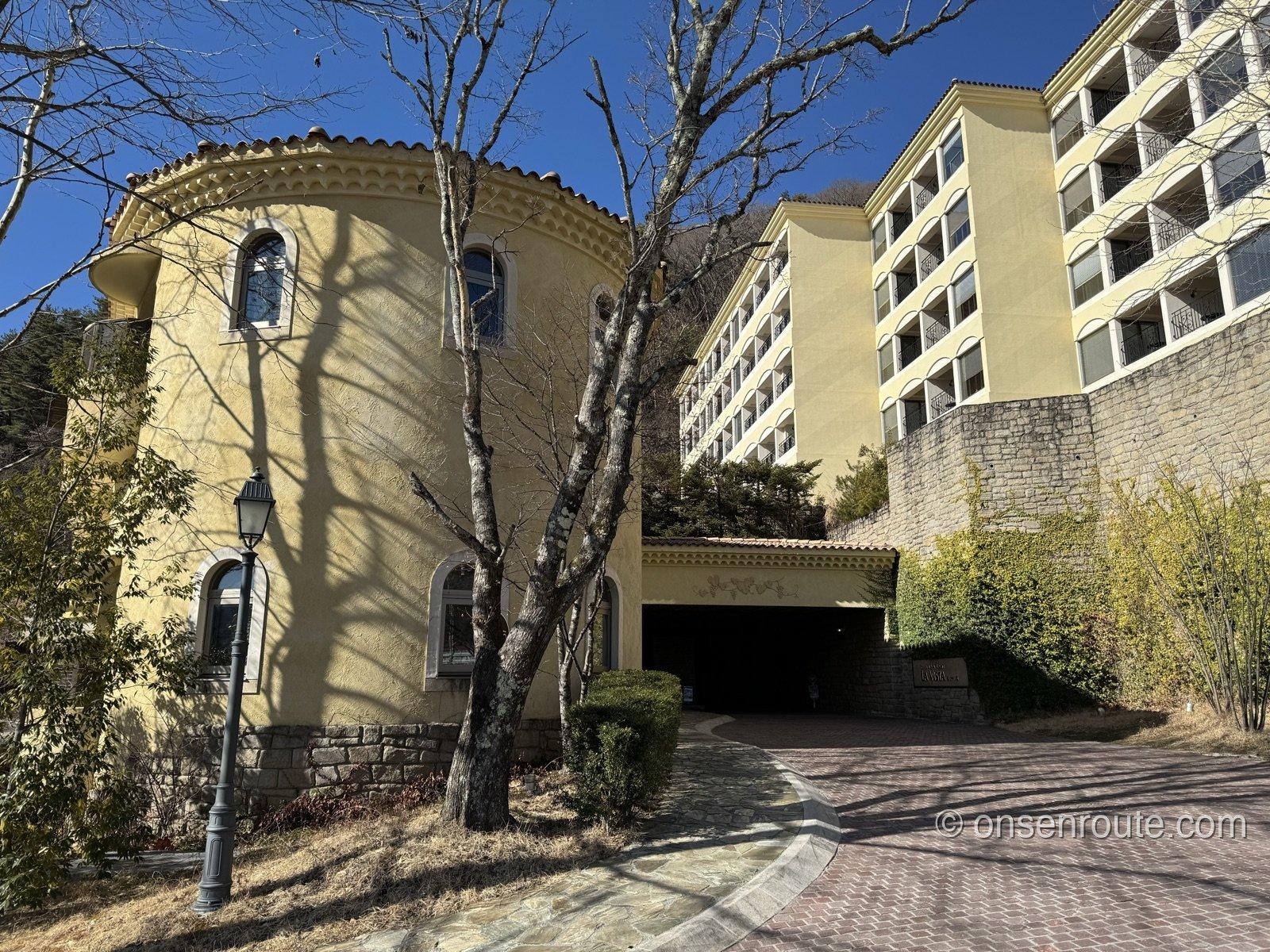 オレンジ色の瓦屋根と黄色い壁のラビスタ富士河口湖の建物。冬の青空と針葉樹の山を背にアーチ状のバルコニーが並ぶ