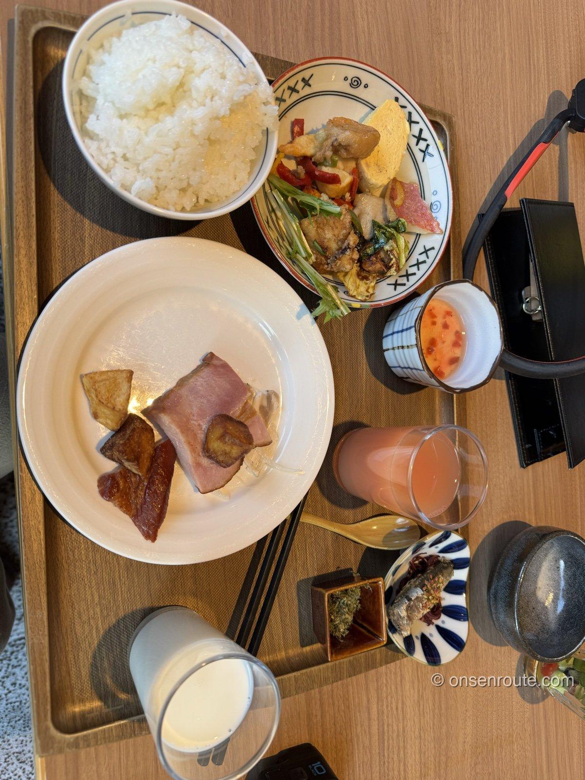 里海の朝食ビュッフェを盛った膳。白飯、ハムとベーコン、野菜の炒め物の小鉢、ジュース、牛乳、佃煮