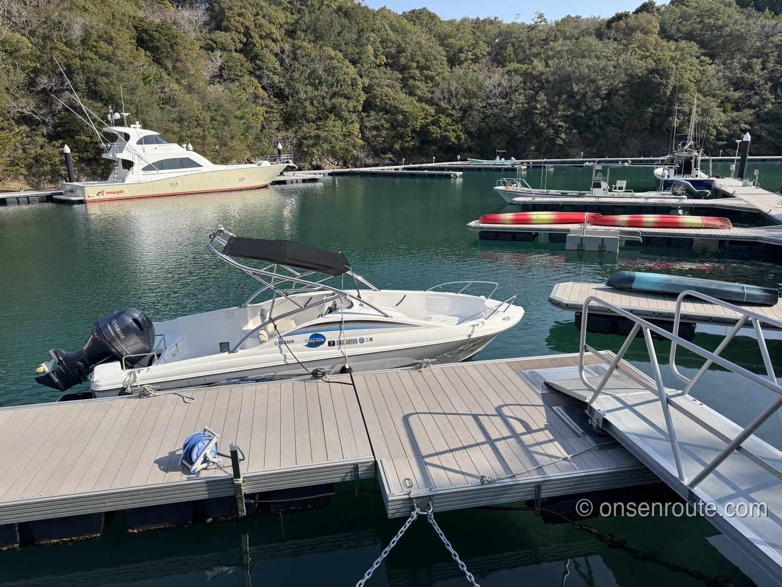 NEMU RESORTのマリーナ。浮き桟橋にモーターボートが係留され、奥にクルーザーと赤いカヤック、緑の岬