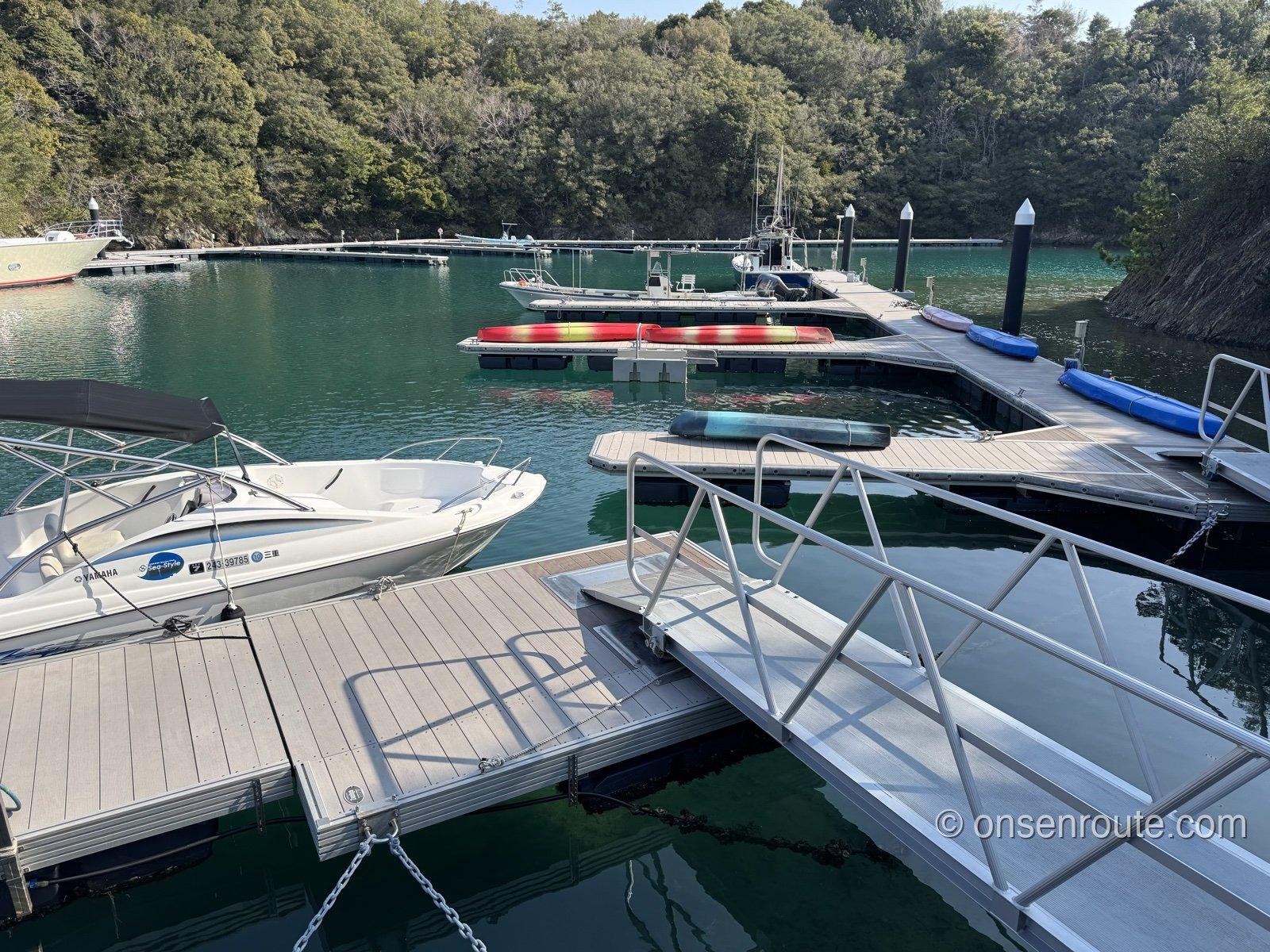 マリーナの浮き桟橋と手すり。緑がかった水面にボート、赤いカヤックとSUPが並ぶ