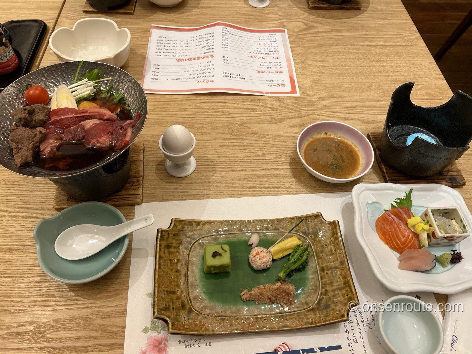 大川荘の夕食。前菜の盛り合わせ、サーモンの刺身、固形燃料にかけられた馬肉のすき焼き鍋が並ぶ