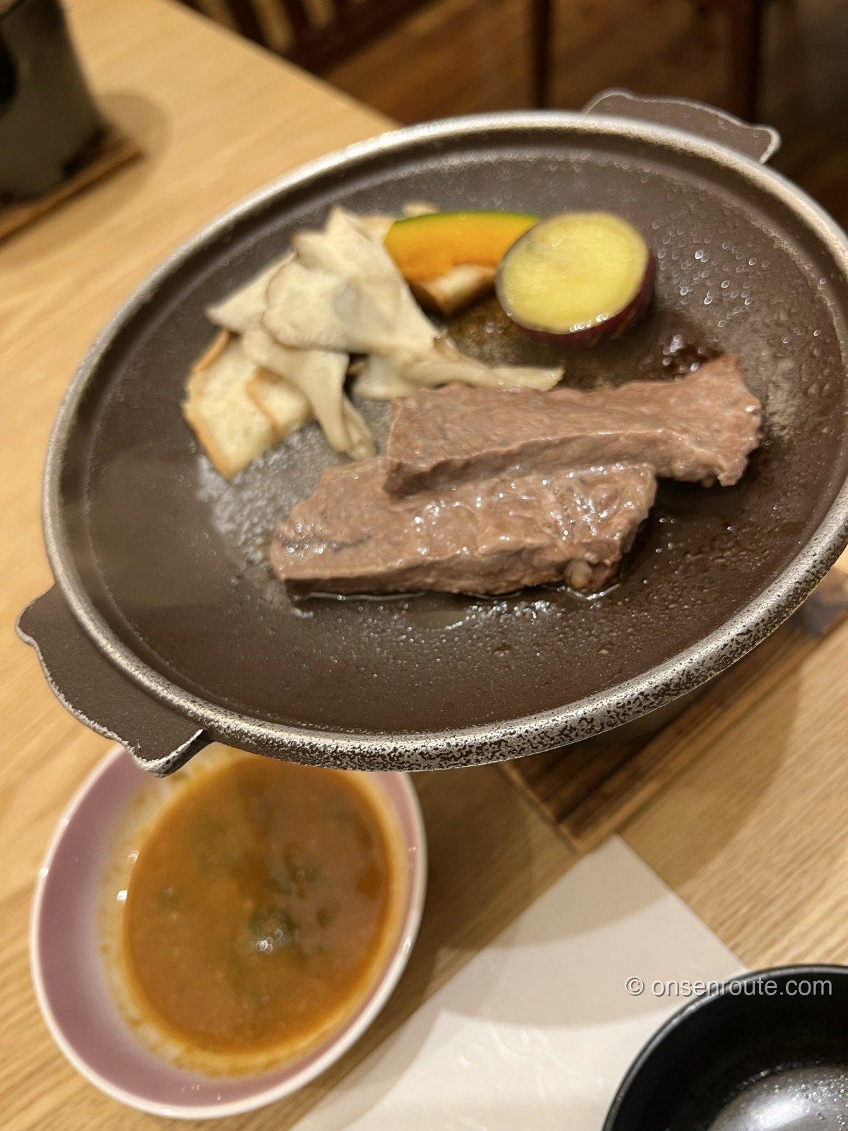 陶板の上で焼かれる牛肉。付け合わせに舞茸、かぼちゃ、さつまいもが添えられている