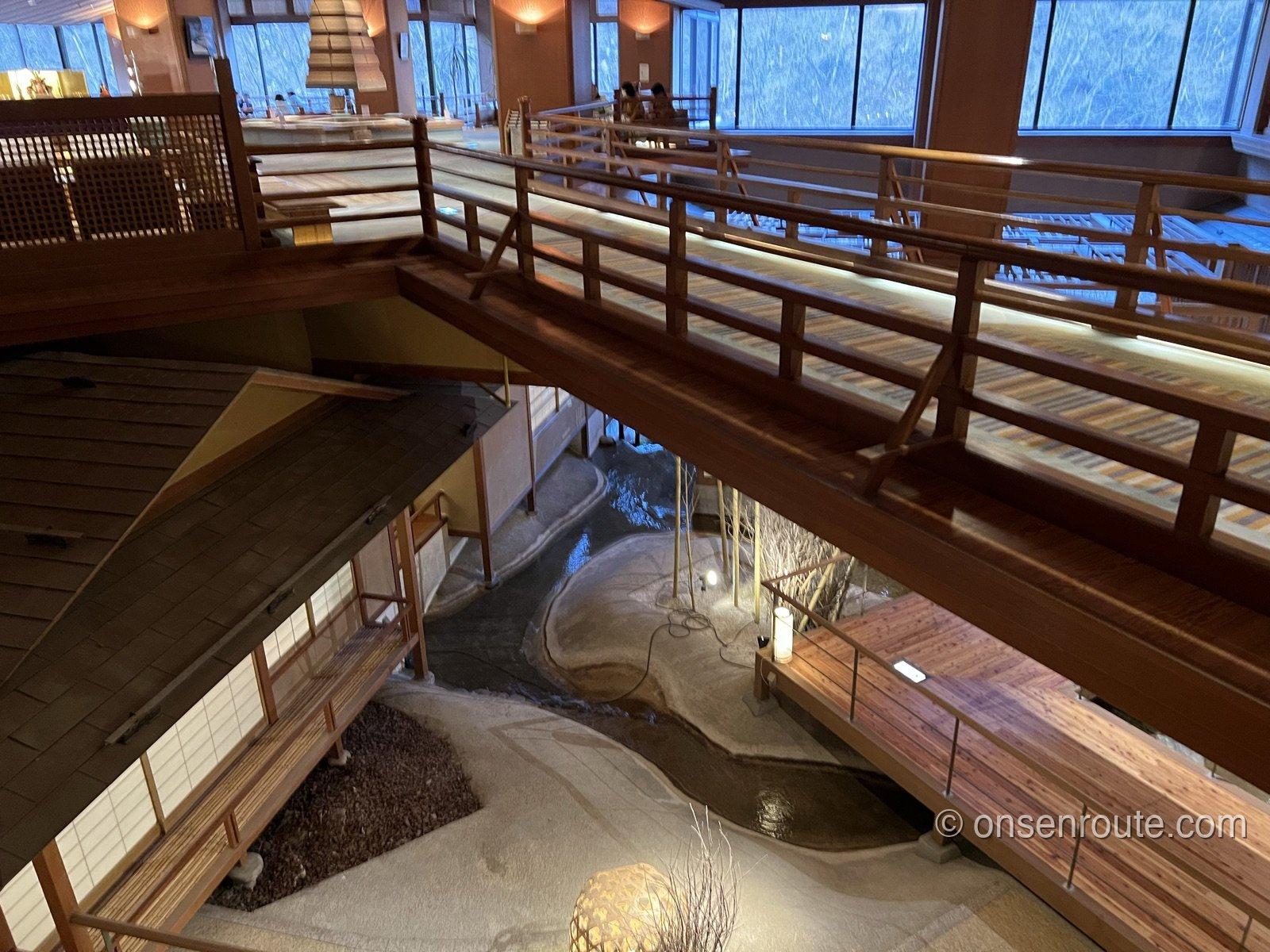 大川荘の吹き抜けを見下ろした眺め。木の橋のような通路の下に、水盤と茶室風の建物が見える