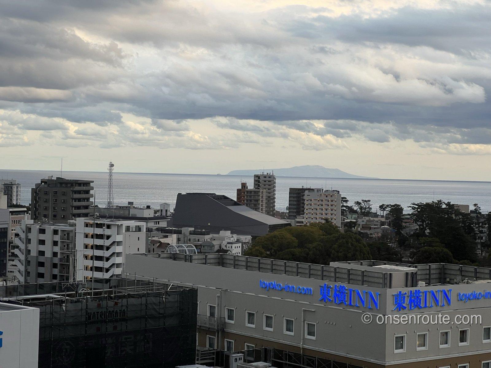 部屋の窓から見た小田原の街並みと相模湾。水平線に伊豆大島のシルエットが浮かぶ