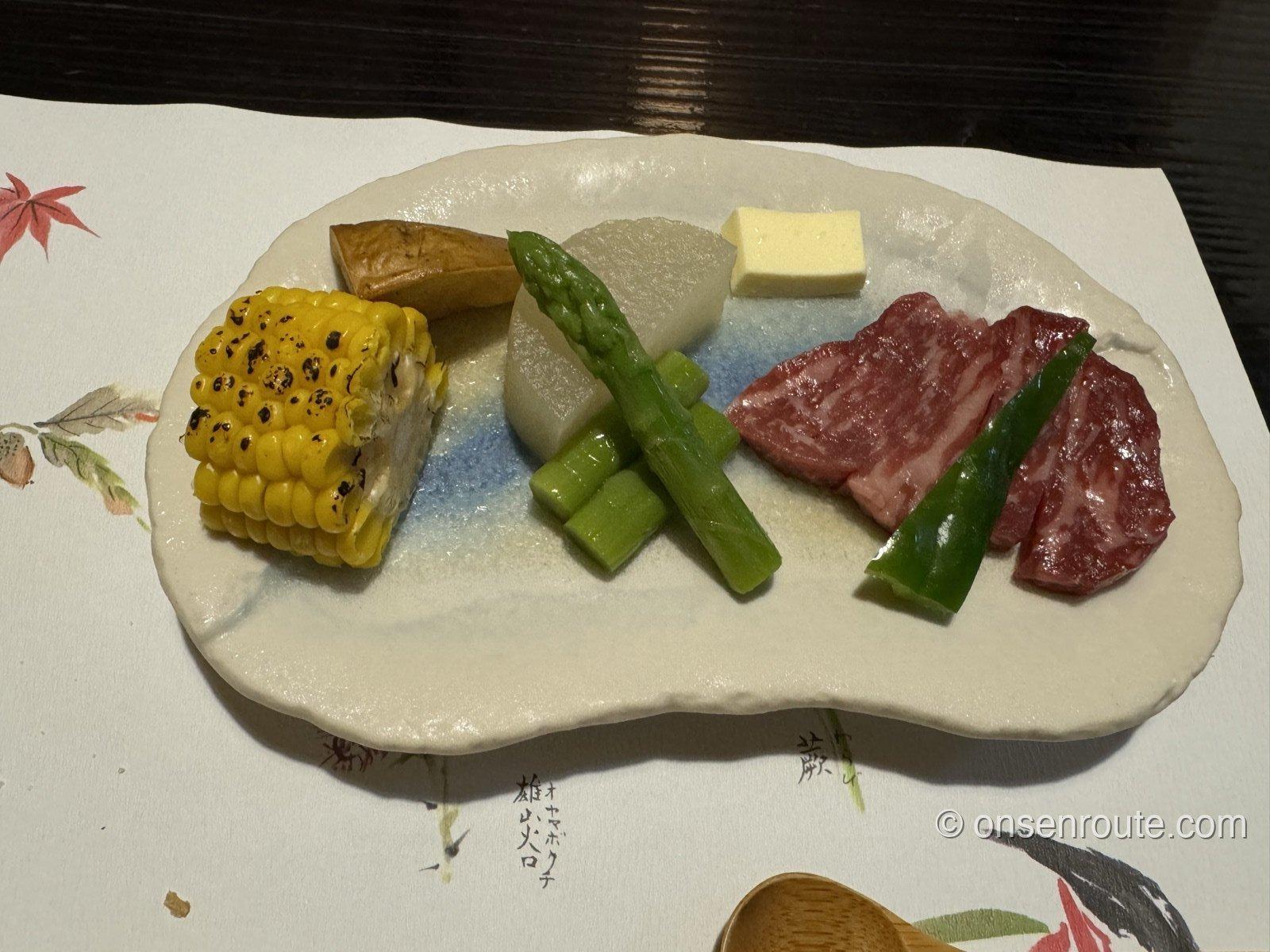 白い陶板の上の肥後牛と野菜。とうもろこし、アスパラ、大根、バターが彩りよく並ぶ