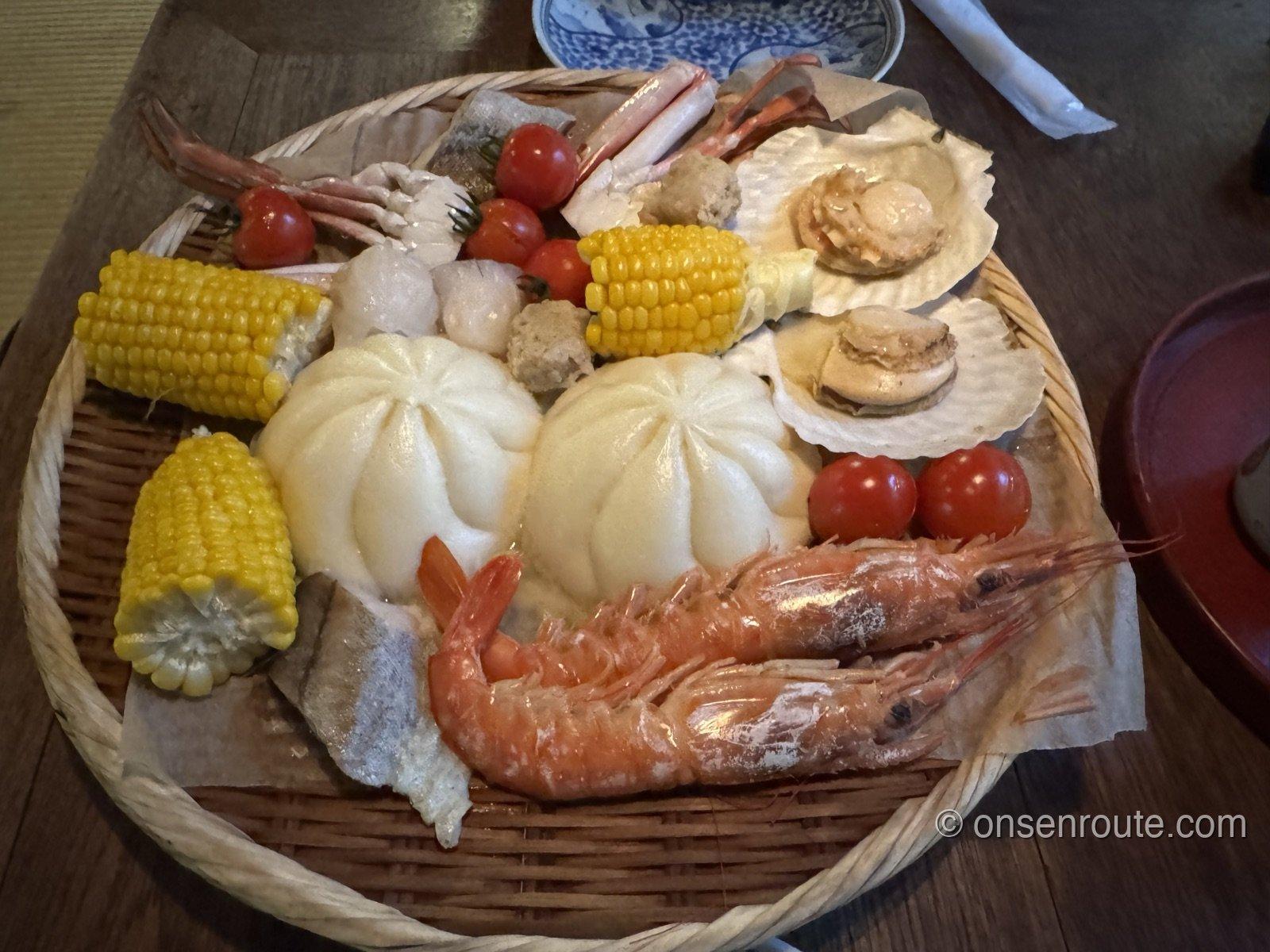 蒸す前の食材が入った籠。海老、蟹、帆立、肉まん、とうもろこし、ミニトマトが並ぶ