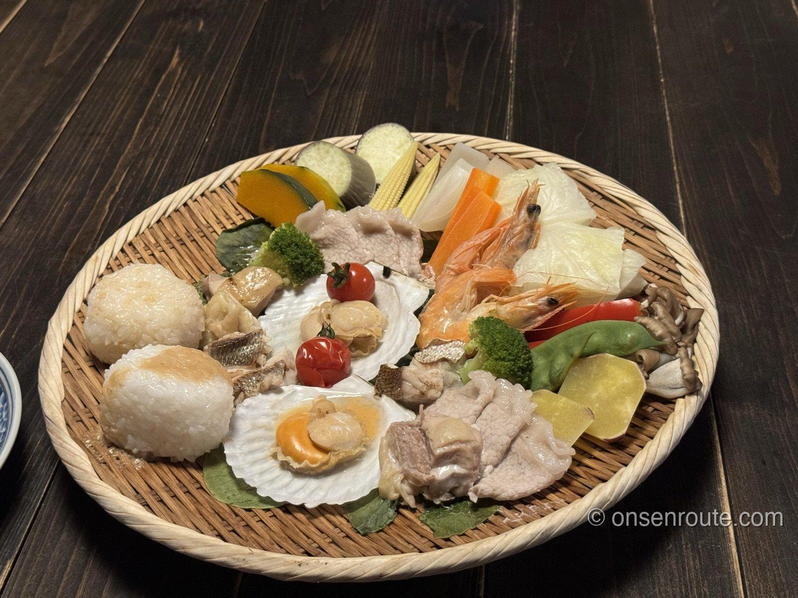 蒸し上がった地獄蒸しセット。ざるに帆立、海老、豚肉、とうもろこし、かぼちゃなどが彩りよく並ぶ