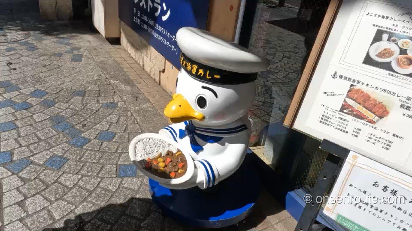 横須賀海軍カレー本舗の店頭に立つセーラー服姿のマスコット。カレー皿を持って出迎えている