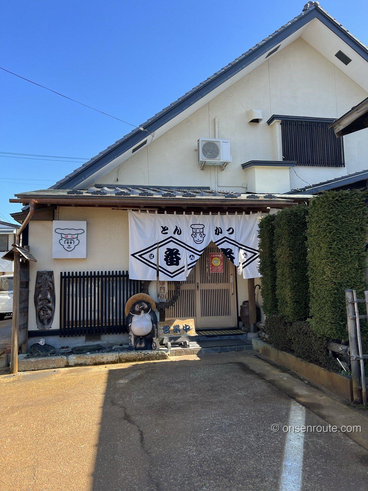 とんかつ番番の外観 白い蔵造り風の建物にとんかつ番番ののれんとたぬきの置物