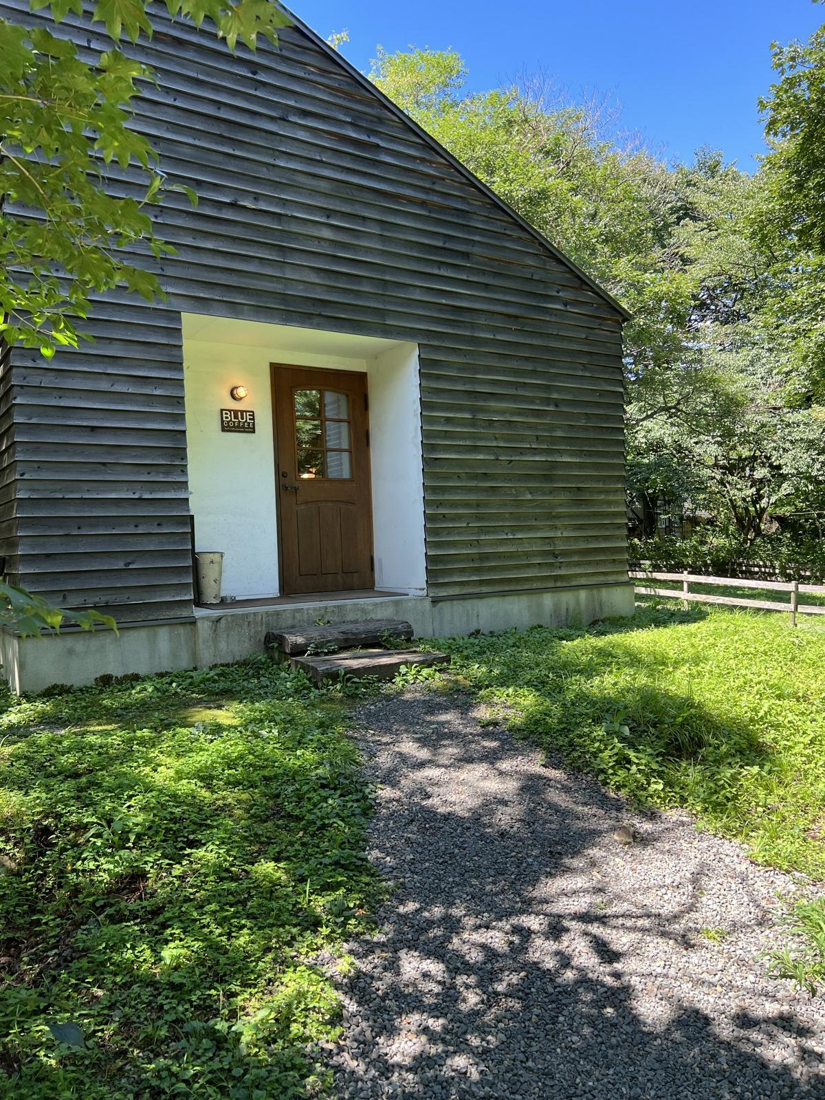 森の木立の中に建つBLUE COFFEEの板張りの建物。白い入口の脇に小さなBLUEの看板