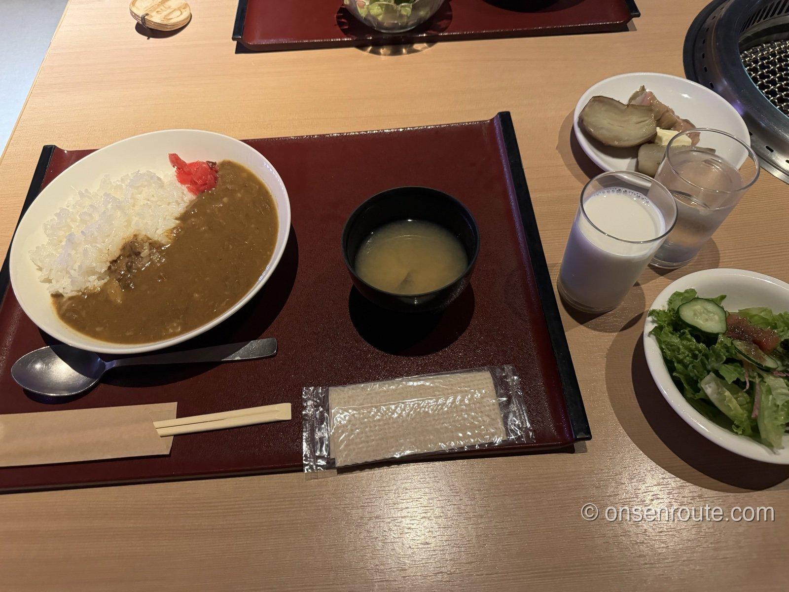 朱色の膳にのった朝食。大きめの皿にご飯とカレー、福神漬け、味噌汁が並び、脇にサラダと牛乳、じゃがいもの小鉢が置かれている