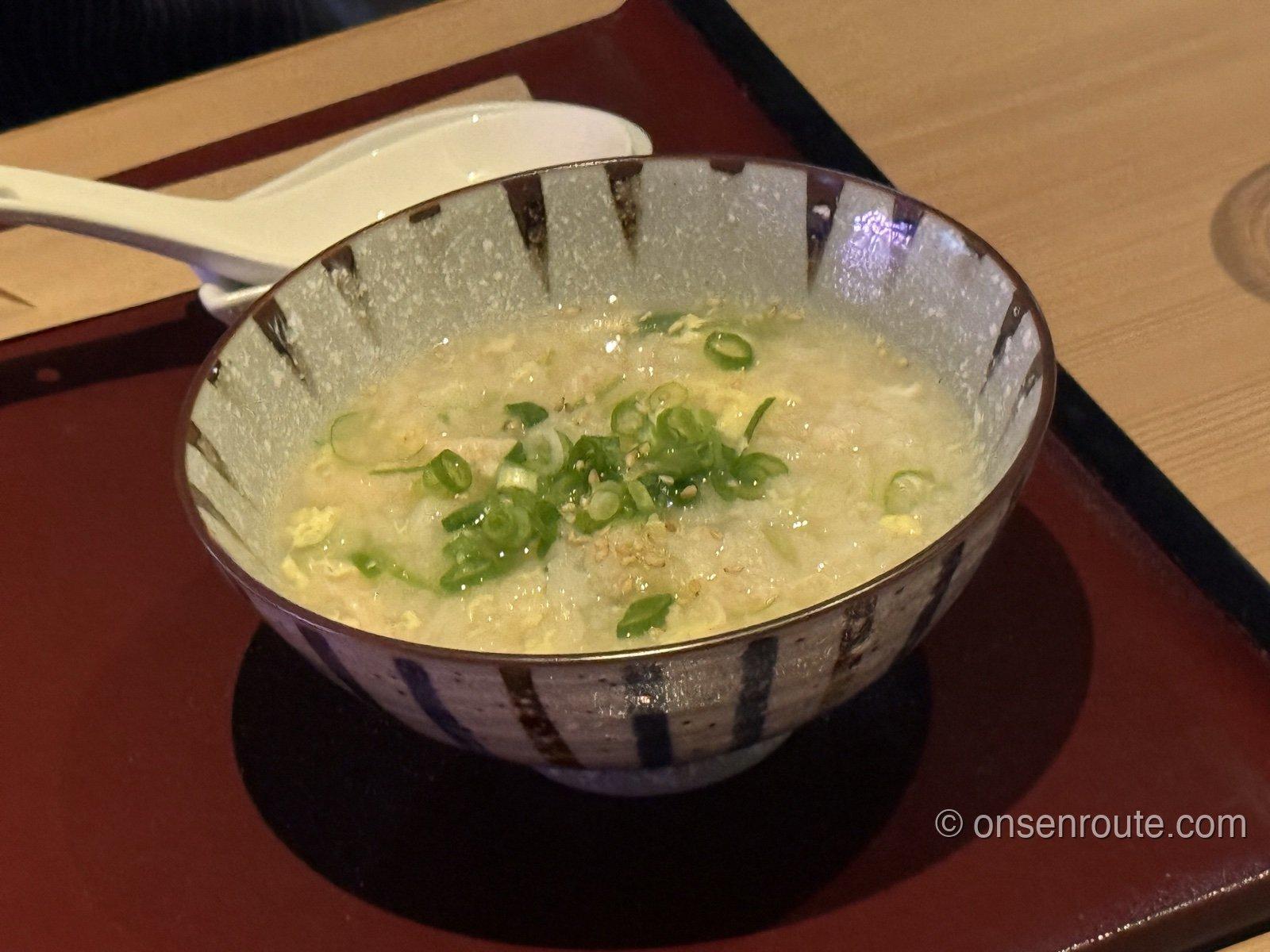 刷毛目模様の茶碗によそわれた雑炊。溶き卵ととろみのある汁に、刻んだ青ねぎと白ごまが散らしてある