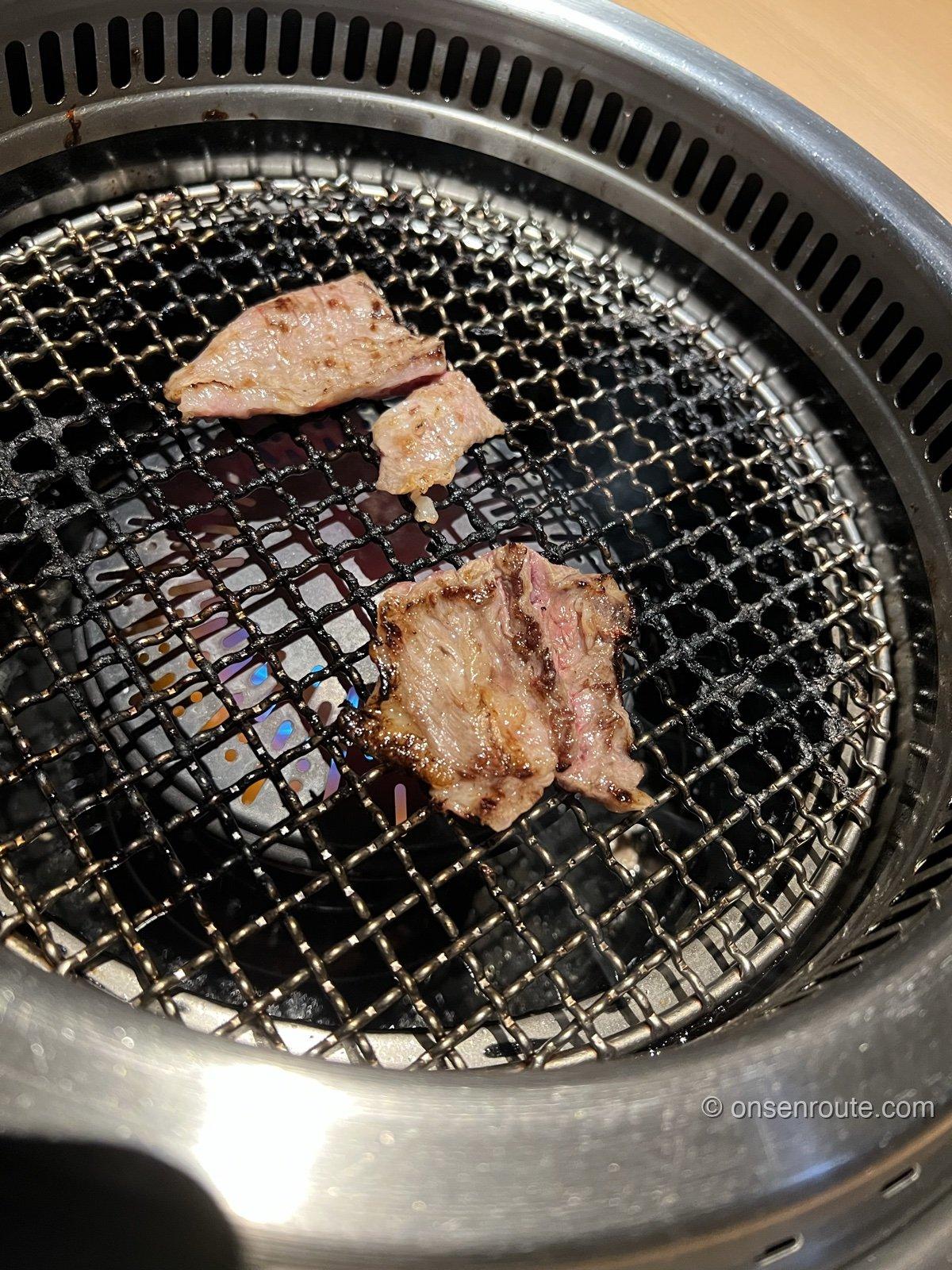 七輪の網の上で焼かれる牛肉。3切れの肉に焼き色がつき、網の下から炎が見える