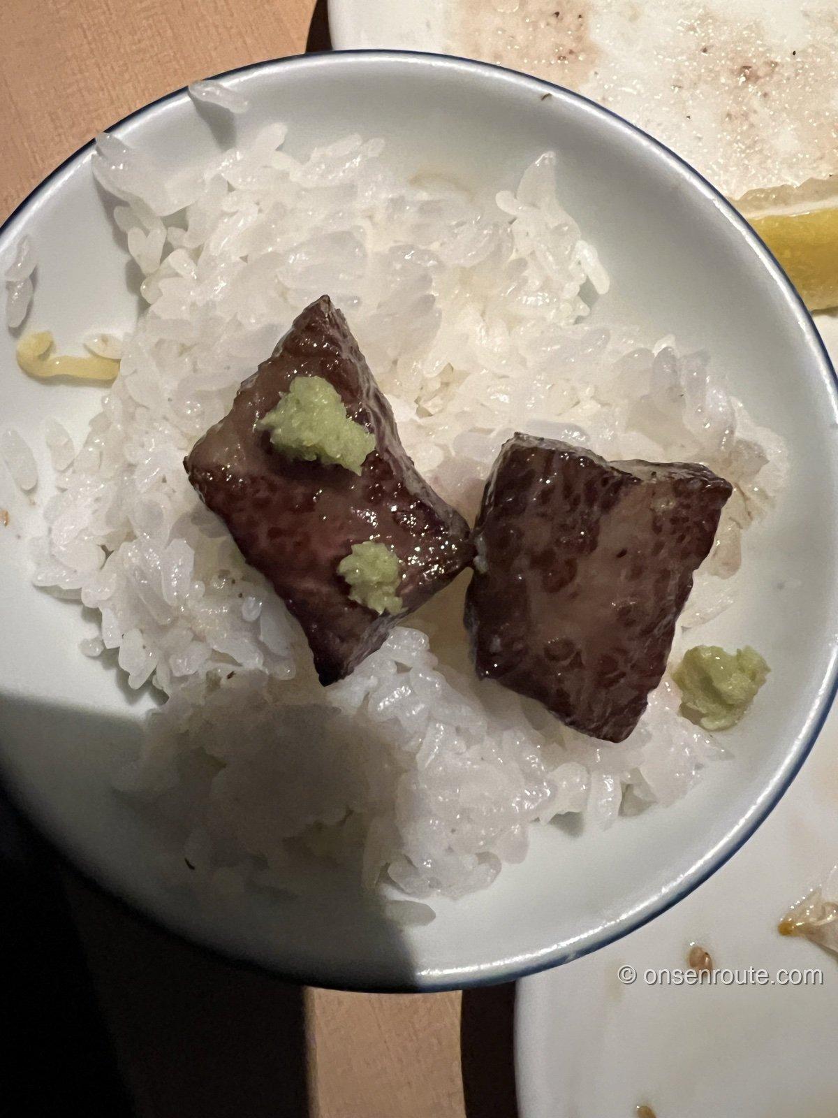 白いご飯を盛った小ぶりの茶碗に、焼いた厚切りの肉が2切れのせられ、わさびが添えられている