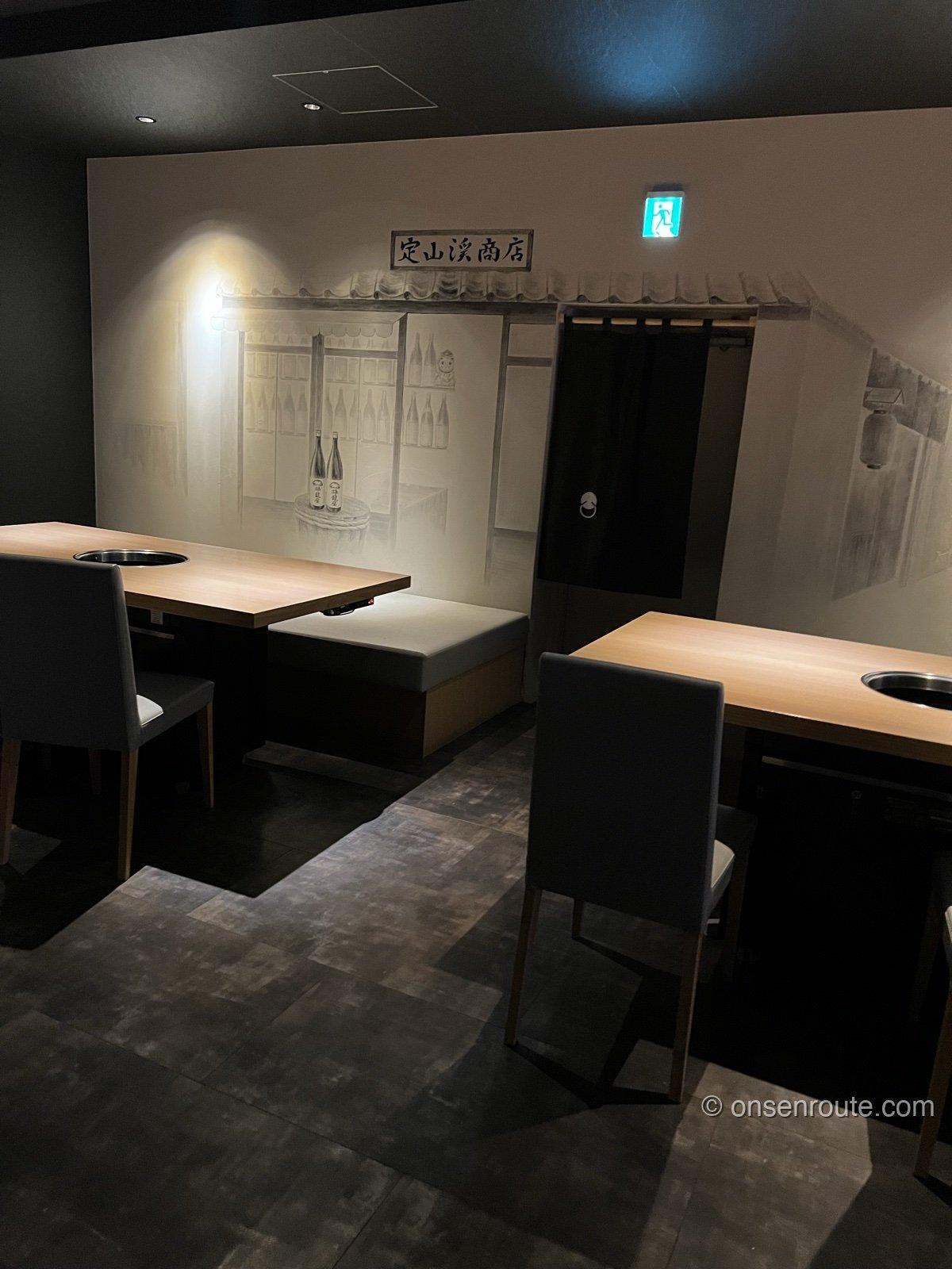 焼肉店「定山渓精肉店」の店内。壁一面に酒屋を描いた墨絵と「定山渓商店」の看板があり、七輪を落とし込んだ木のテーブルが並ぶ