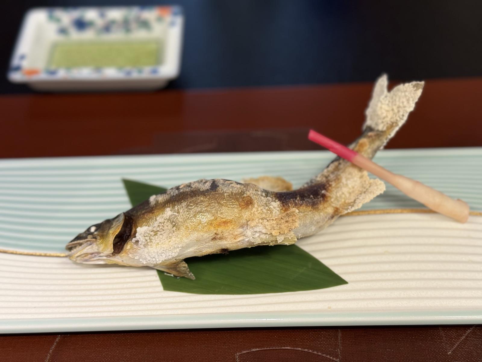 人吉旅館の夕食。笹の葉の上に鮎の塩焼き、奥に緑色のたれ