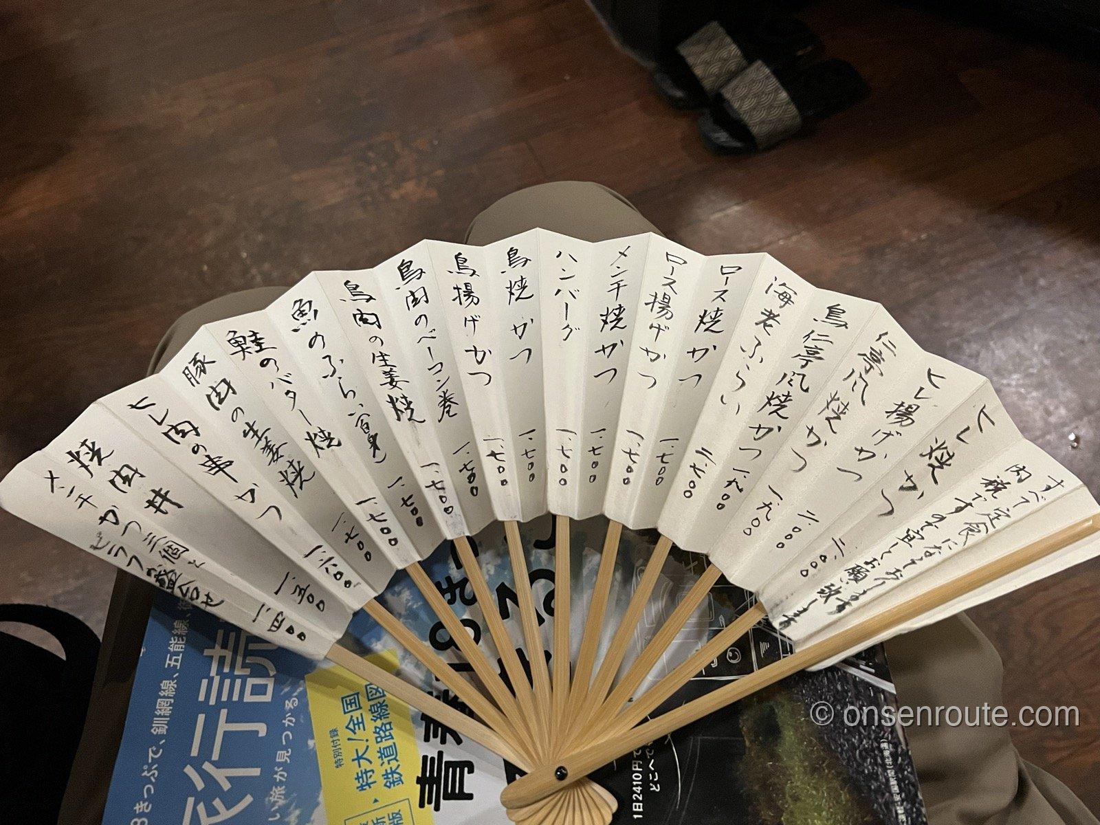 仁亭のメニュー 扇子に手書きでロース焼かつやヒレ焼かつなどの品書きが書かれている
