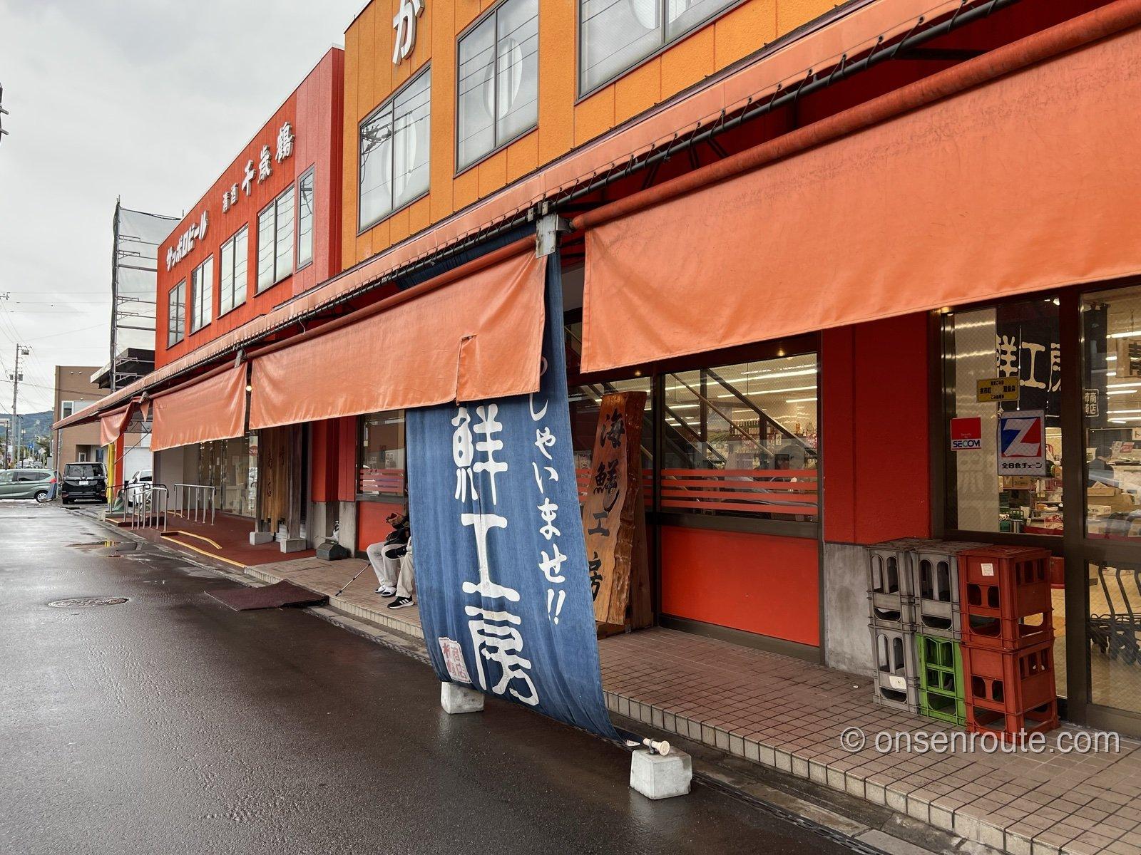 余市駅前の柿崎商店の外観。オレンジのひさしの下に海鮮工房の紺色ののぼりが立つ