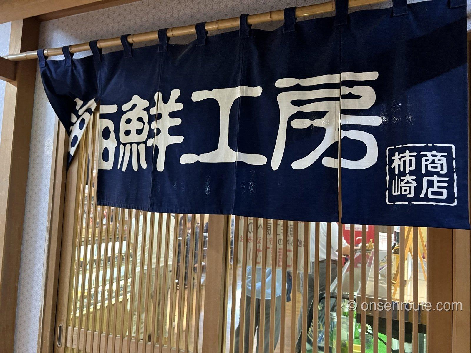 海鮮工房の入口にかかる紺色の暖簾。白抜きで海鮮工房、柿崎商店の文字