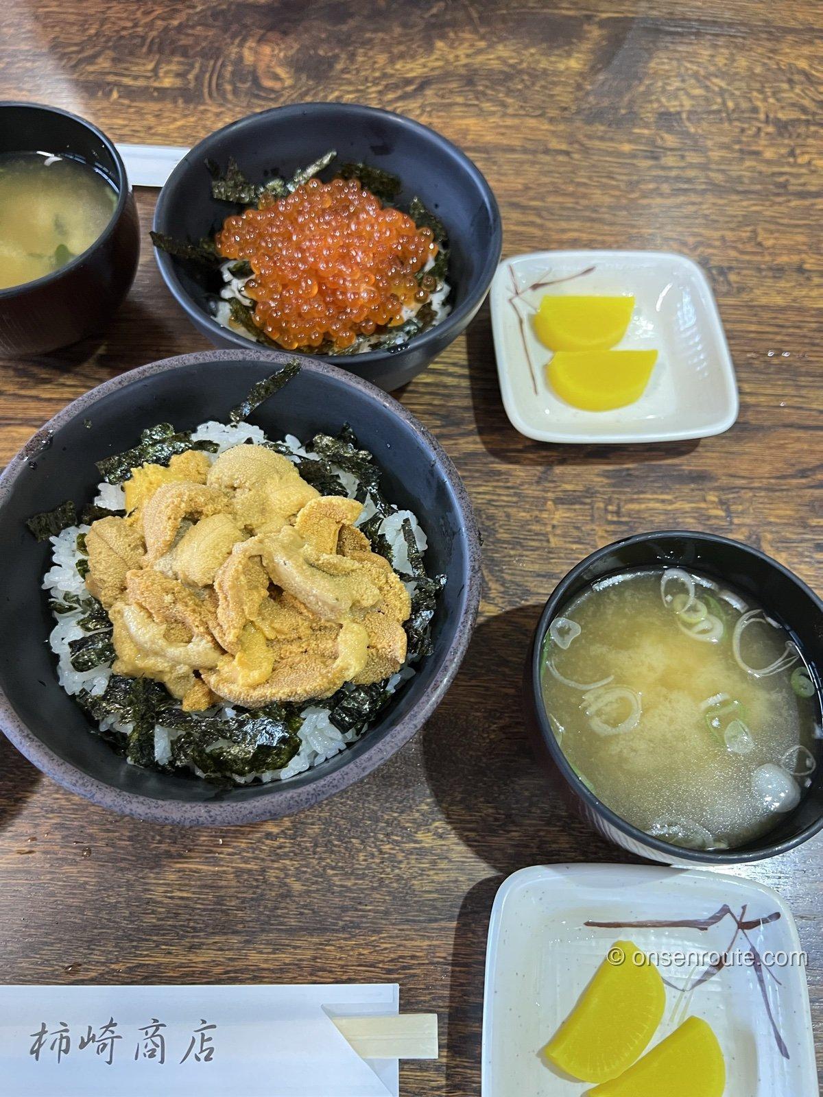 柿崎商店海鮮工房のうに丼といくら丼。黒い丼に山盛りのうにといくら、味噌汁と漬物つき