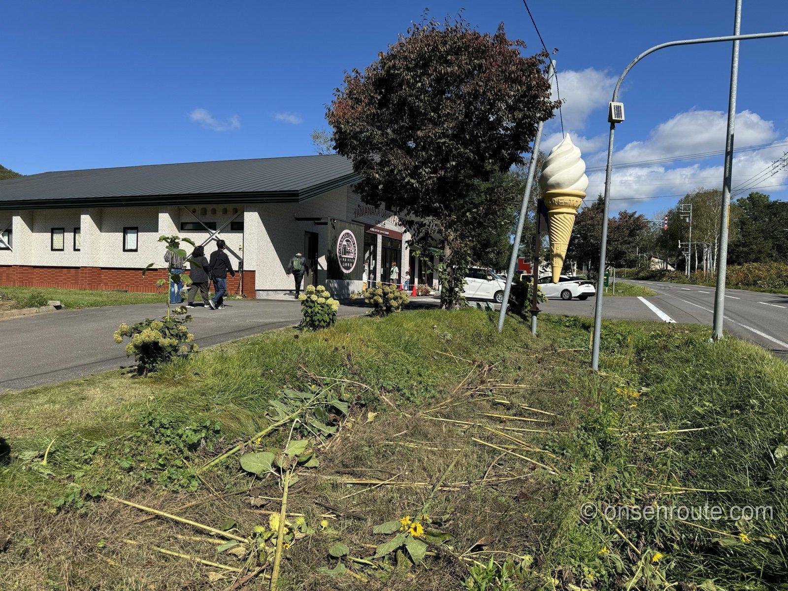 国道393号沿いの山中牧場直売所。ソフトクリームの立体看板と白い建物、青空と秋の木々