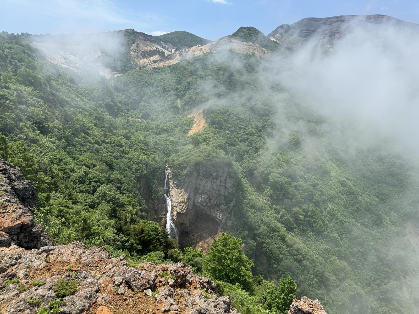 駒草平の展望台から見る不帰の滝。緑の谷に白い一筋の滝が落ち、山肌に雲がかかる