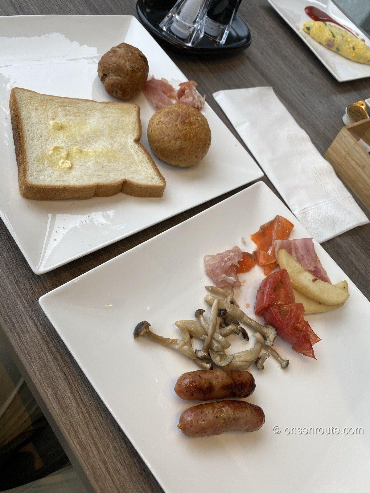 朝食ビュッフェの盛り付け。トーストとパン、生ハム、ソーセージ、きのこのソテー、トマト