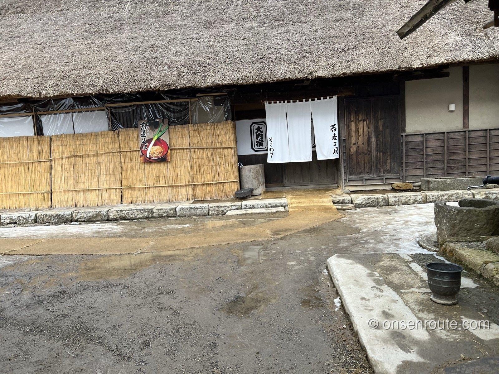 大内宿三澤屋の茅葺き屋根の店構え 白いのれんとねぎそばの看板