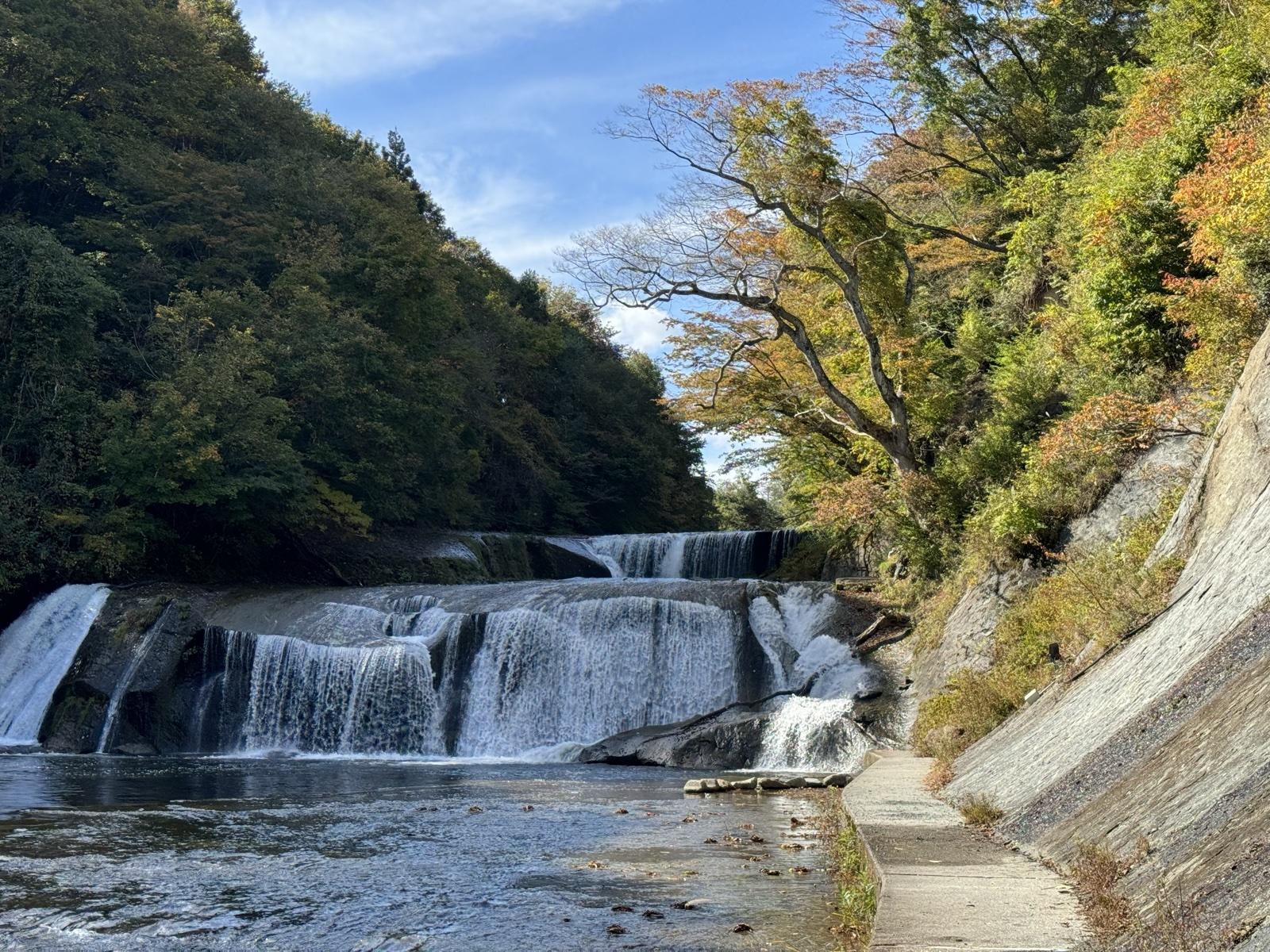 紅葉に囲まれた滑津大滝。幅広の滝が二段に流れ落ち、右手に遊歩道が続く
