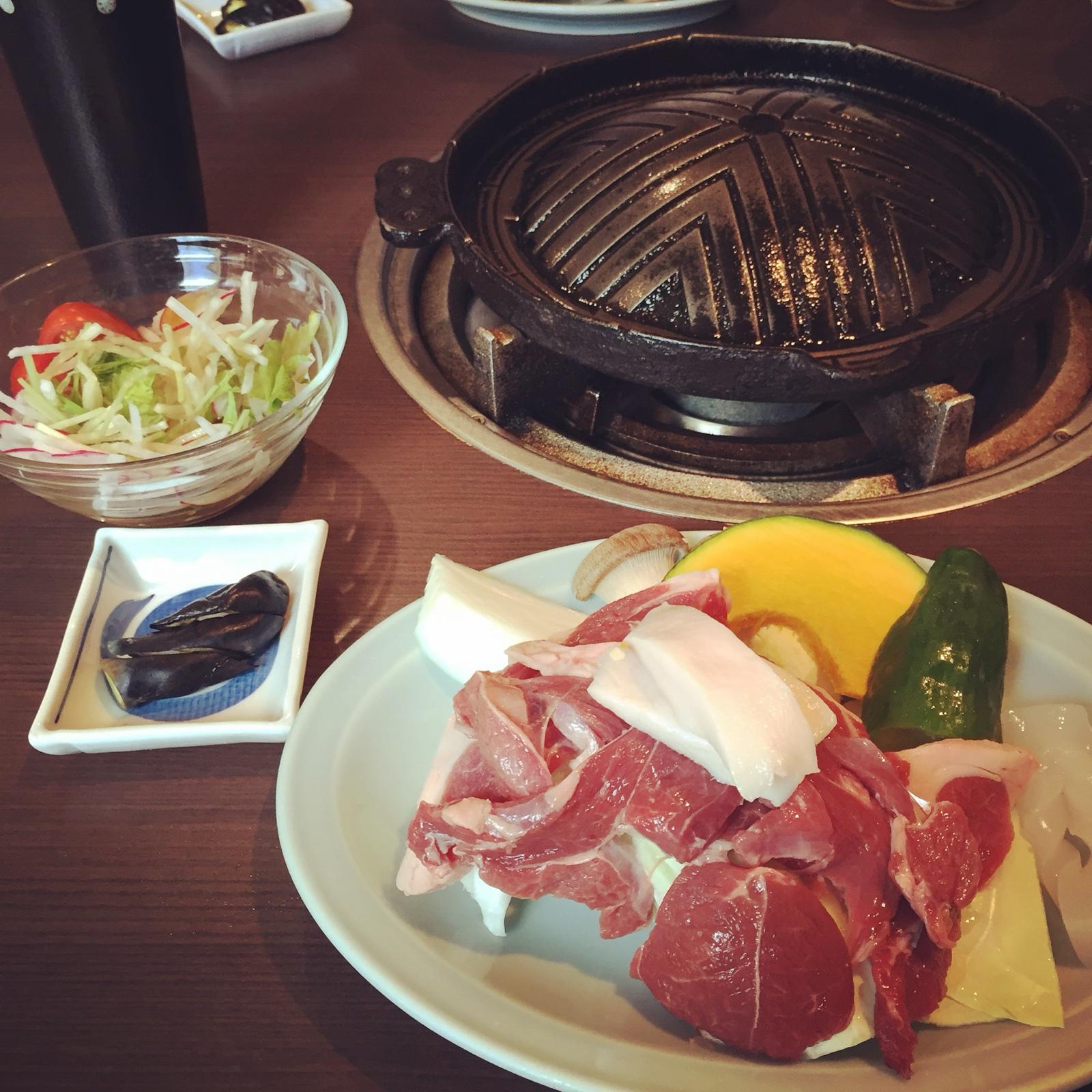 ろばたのジンギスカンセット。皿に盛られたラム肉とかぼちゃ・ピーマンなどの野菜、奥にジンギスカン鍋