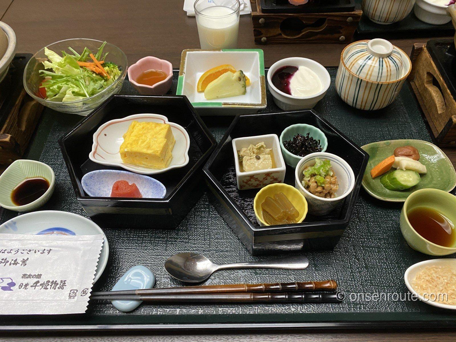 黒いお盆にのった和定食の朝食。出汁巻き玉子、たらこ、湯葉、納豆、サラダ、香の物、ヨーグルト、フルーツなどが小鉢で並ぶ