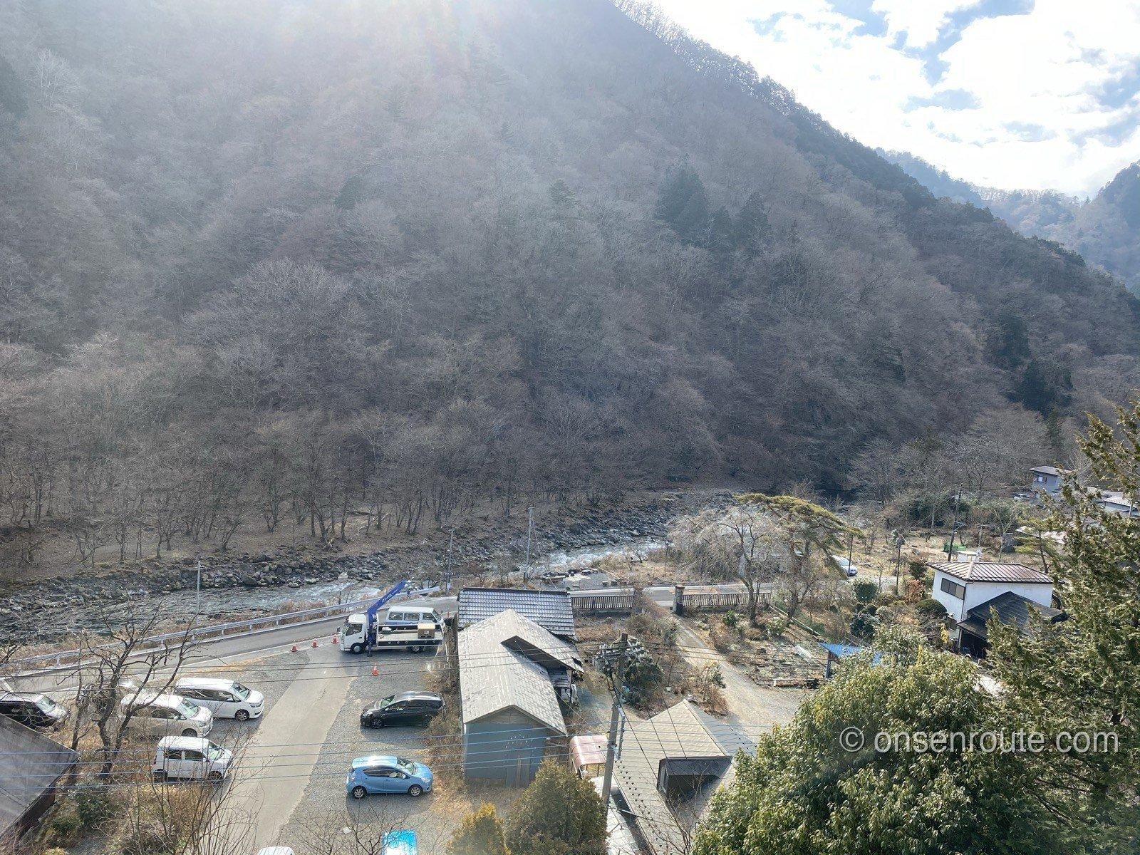 客室の窓から見下ろす大谷川の渓谷。冬枯れの山肌と川、川沿いの道や家並みが見える