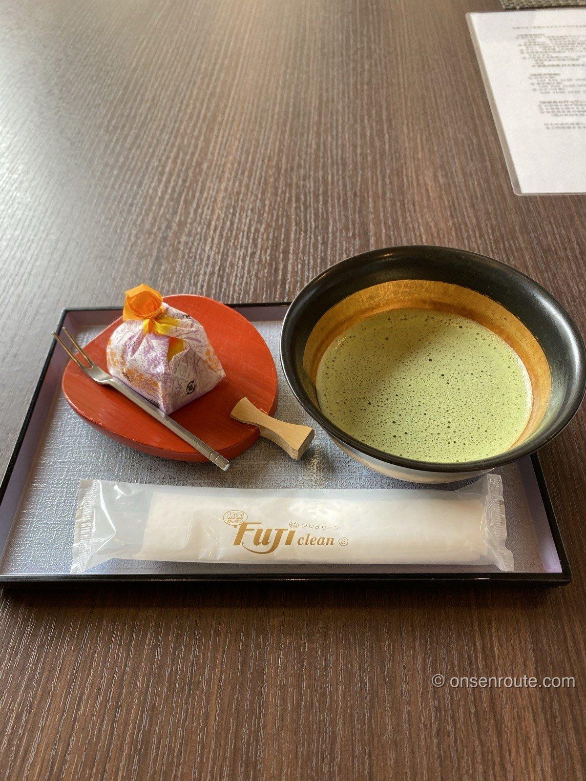 黒い茶碗に点てられた抹茶と、赤い皿にのった包み菓子。黒いお盆にのっている