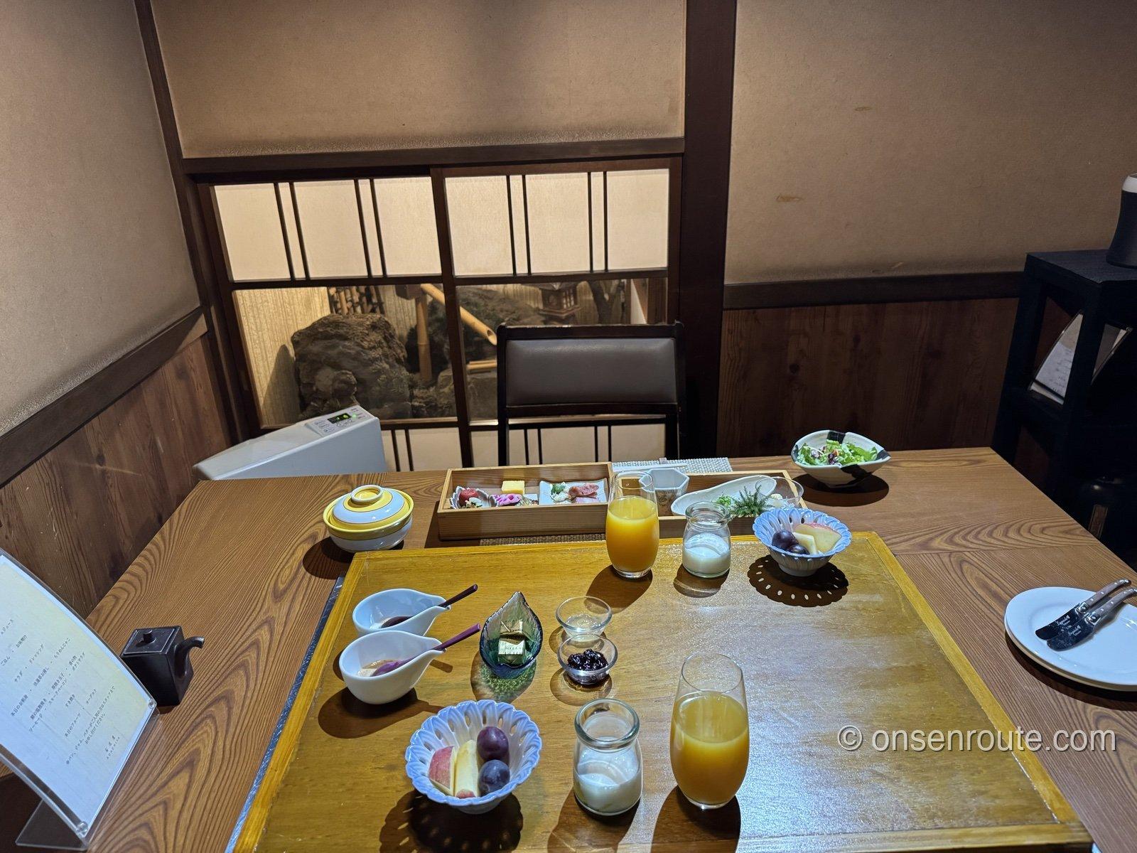 朝食の全景。囲炉裏の台の上にジュースやヨーグルト、ジャムが並び、奥に八寸の箱膳とサラダ