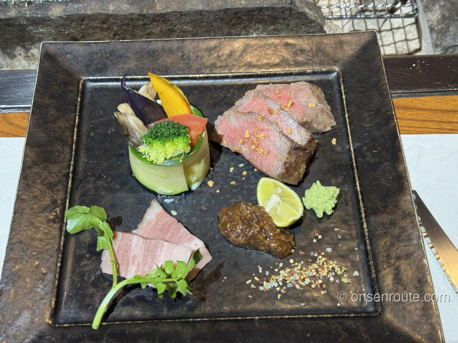 メインの肉料理。黒い角皿にローストした牛肉のスライスと野菜のミルフィーユ仕立て、すだちと薬味が添えられる