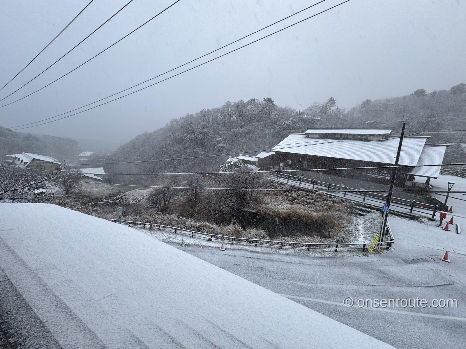 雪の朝の高湯温泉。うっすら雪をかぶった屋根と道路、雪化粧した山々が霞む