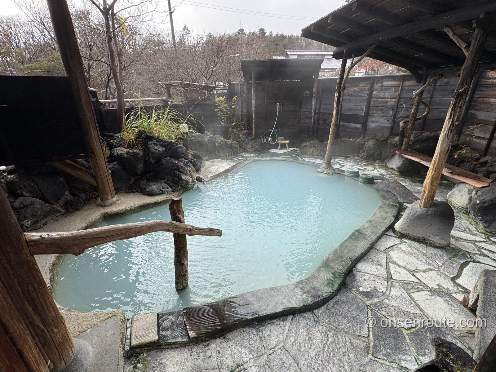 貸切露天風呂「薬師の湯」。青みがかった乳白色の湯をたたえた岩縁の湯船から湯気が立ち、木の柱と石畳が囲む