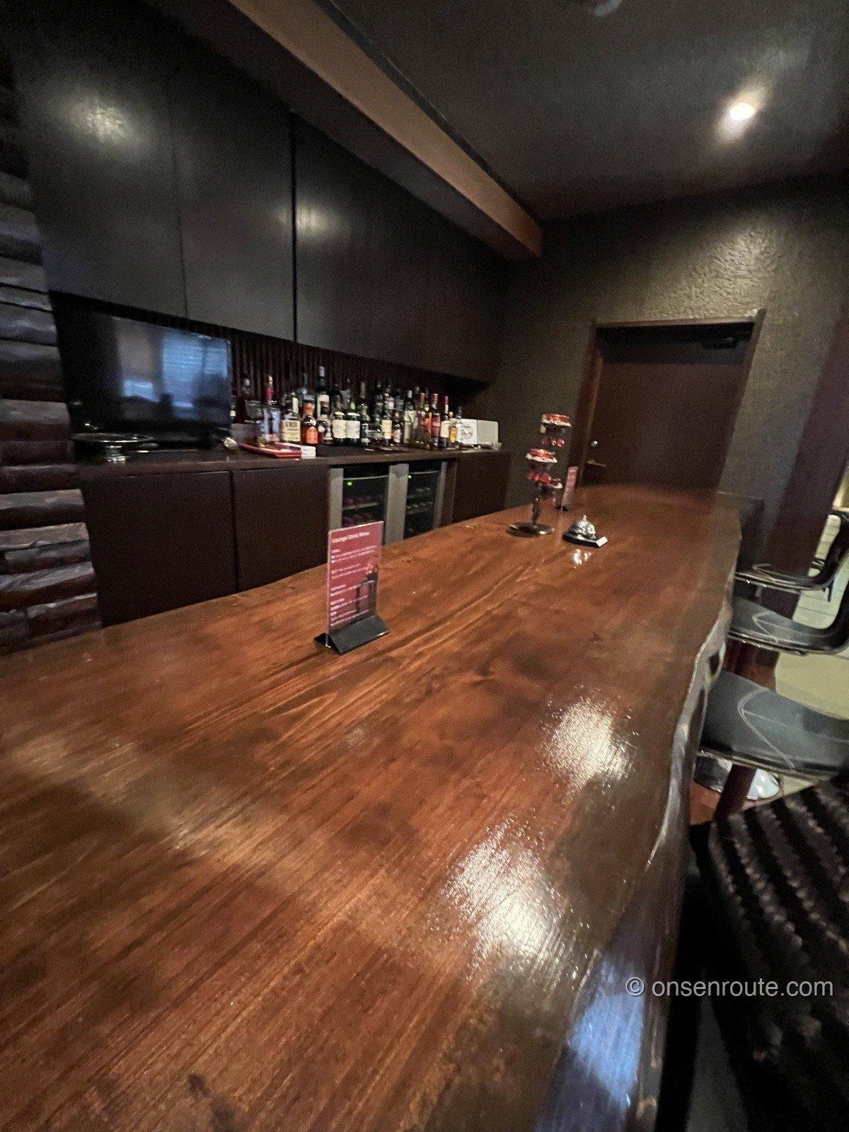 大忠の館内のBAR。一枚板の大きなカウンターの奥に酒瓶の並ぶ棚とワインセラーがあり、ドリンクメニューが置かれている