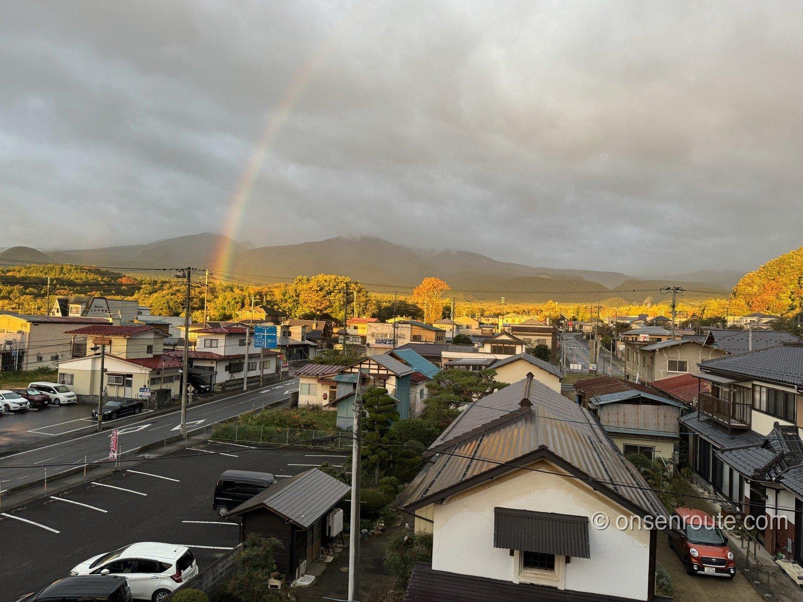 大忠の3階の部屋から見た景色。温泉街の屋根の向こうに紅葉の始まった山並みが広がり、雲のかかった空に虹が架かっている