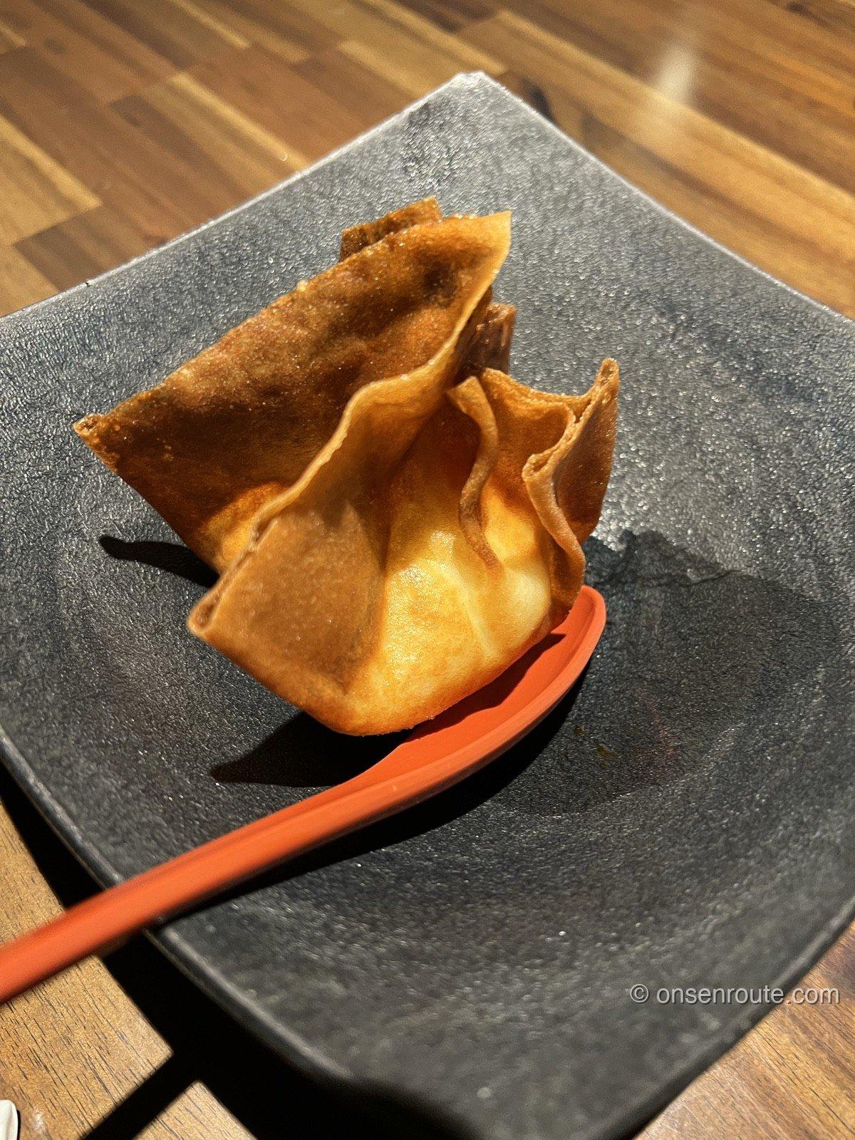 黒い角皿にのった大忠名物の包み揚げ。薄い皮をきんちゃく状に包んで揚げてあり、こんがりと色づいている