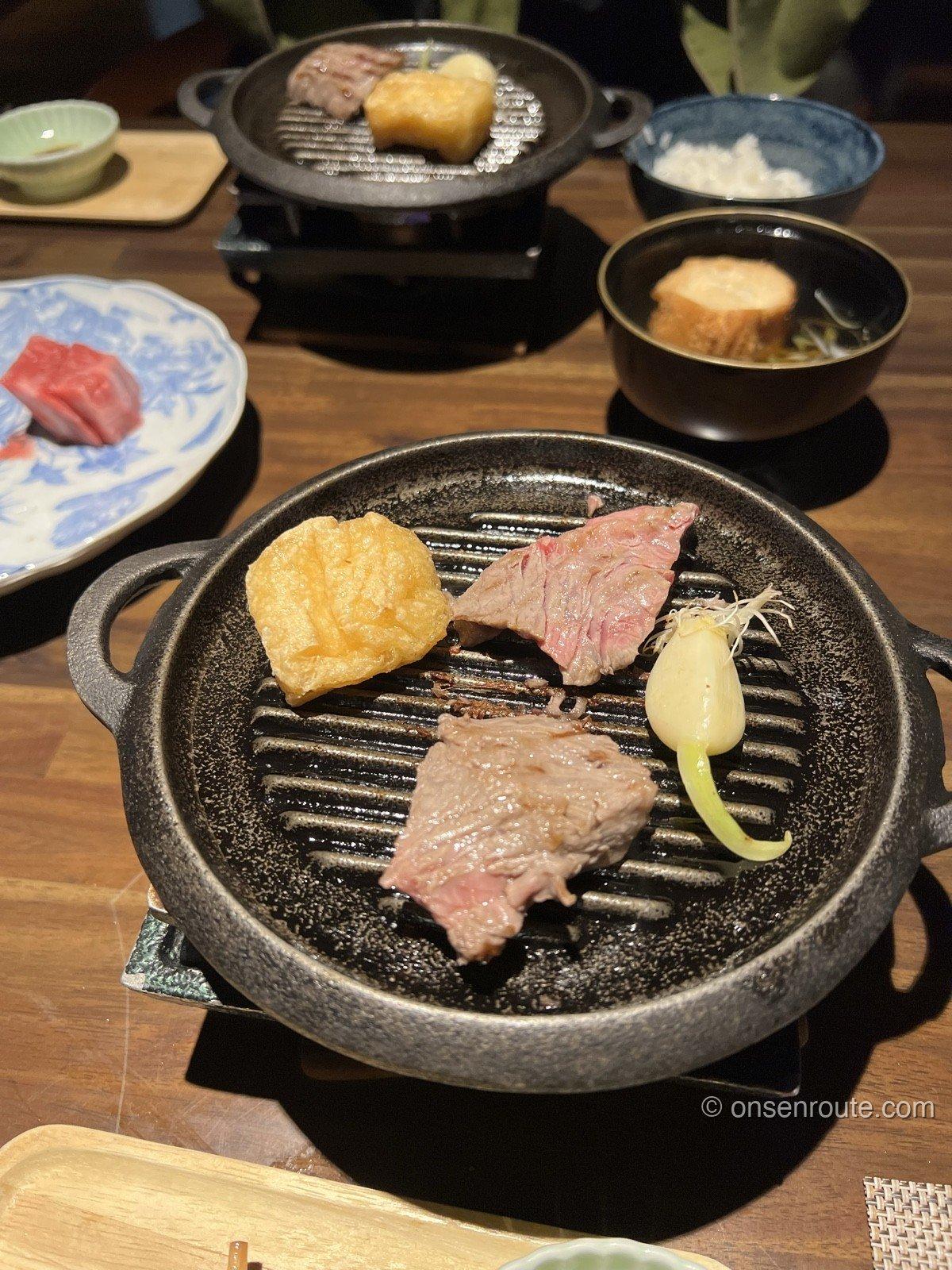 陶板の上で焼かれる蔵王牛のサーロインステーキ。手前にニンニクと厚揚げが一緒にのり、奥に白飯とお椀が並ぶ
