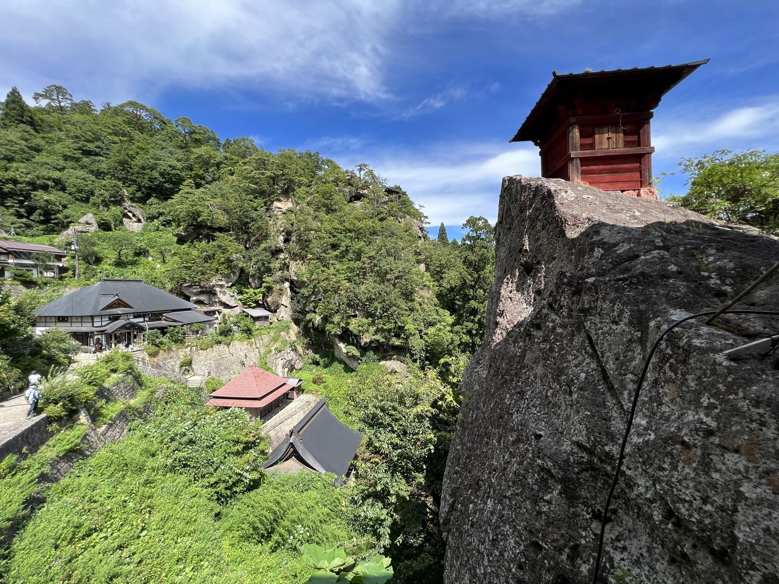 山寺の切り立った岩の上に立つ朱塗りの納経堂。眼下に門前町の屋根が見える