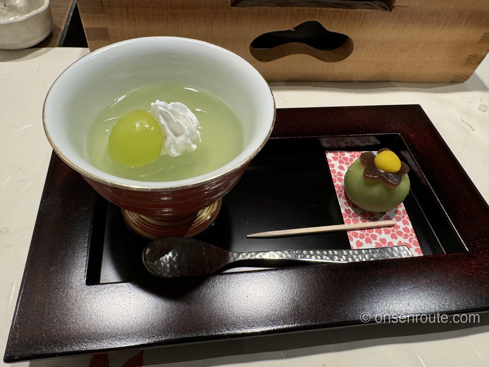 黒い盆にのったデザート。赤い器にシャインマスカットとクリーム、脇に楊枝を添えた小さな菓子